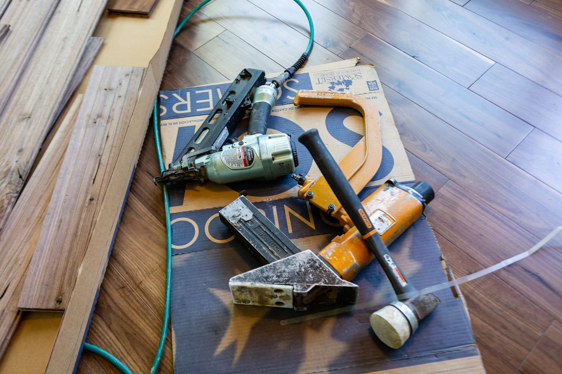 Assorted power tools and hoses piled on a hardwood floor beside a deck railing