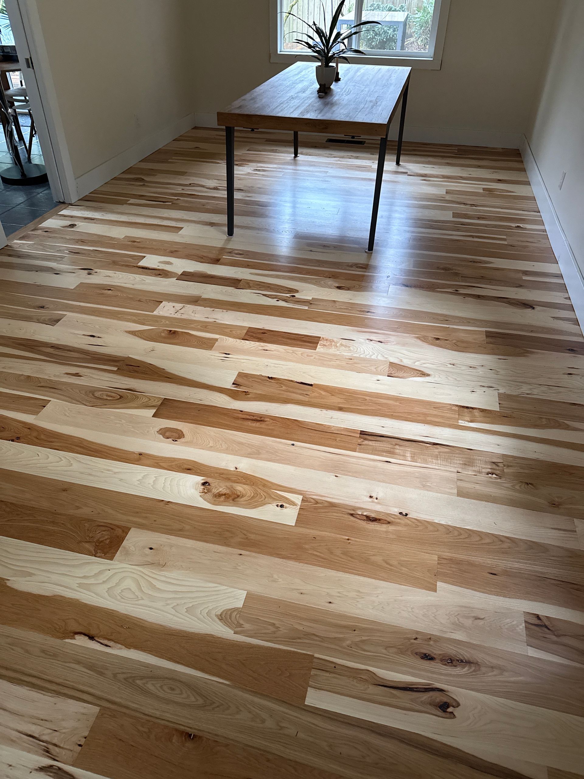Wooden dining table on a newly finished light-and-dark hardwood floor in a sunlit room