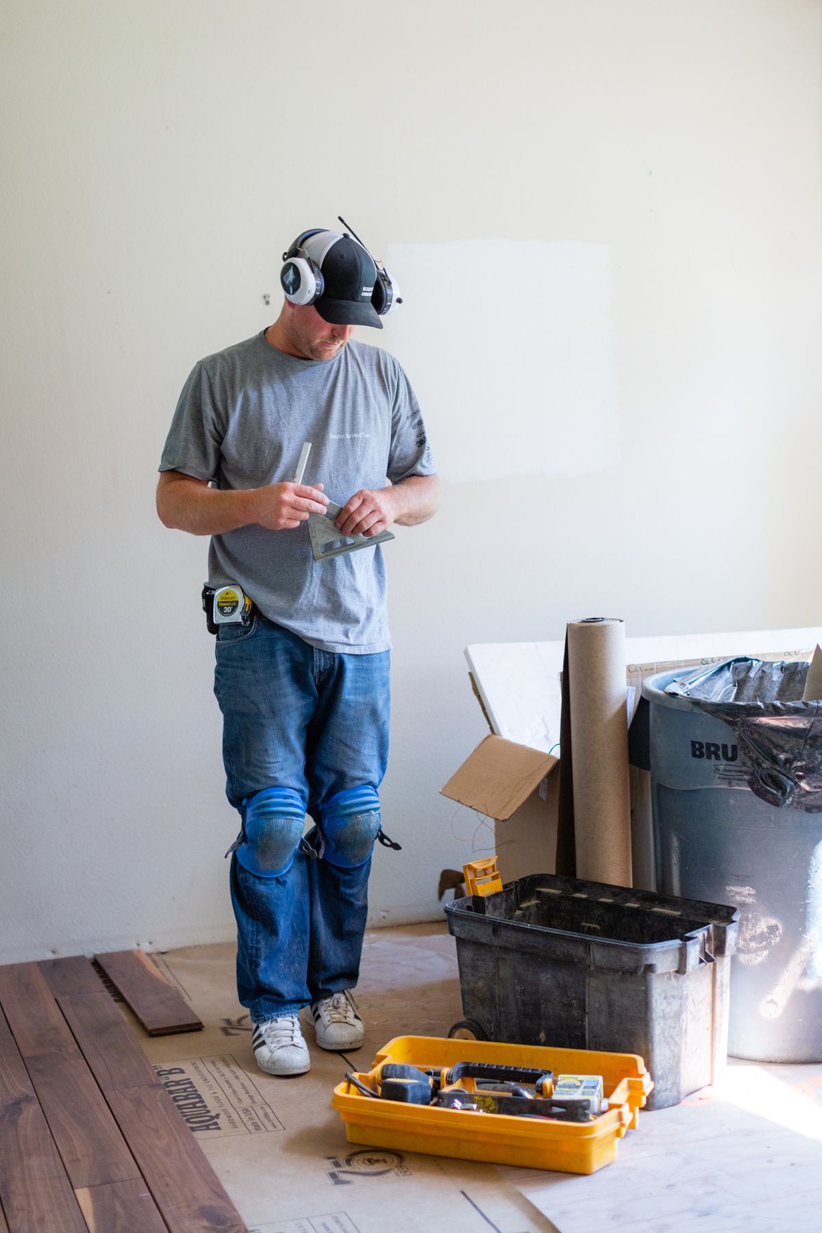 Worker wearing a dust mask measures something in an unfinished room with tools and supplies on the floor
