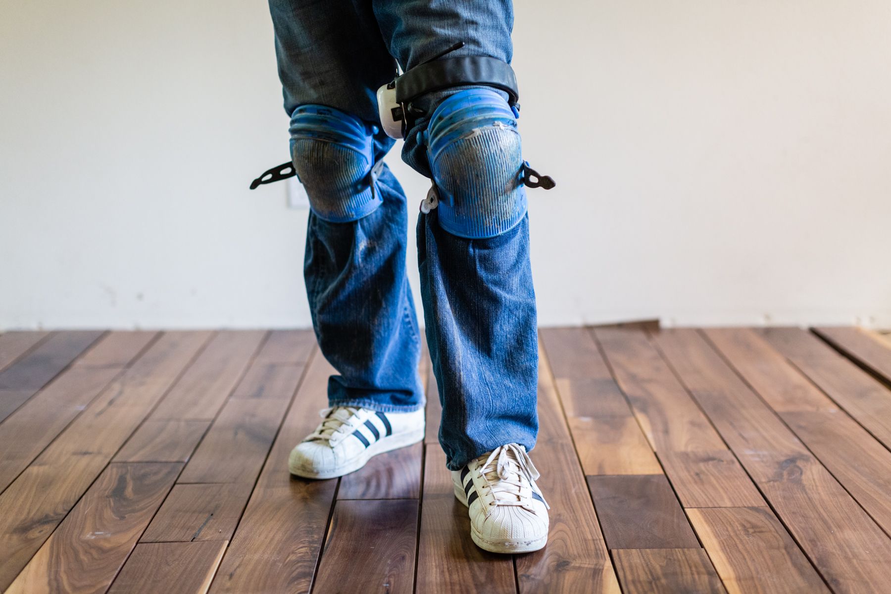 Person wearing blue jeans and white sneakers standing on a wooden floor.