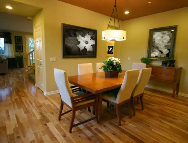 Warm dining room with wooden table, white chairs, pendant light, and framed floral wall art.