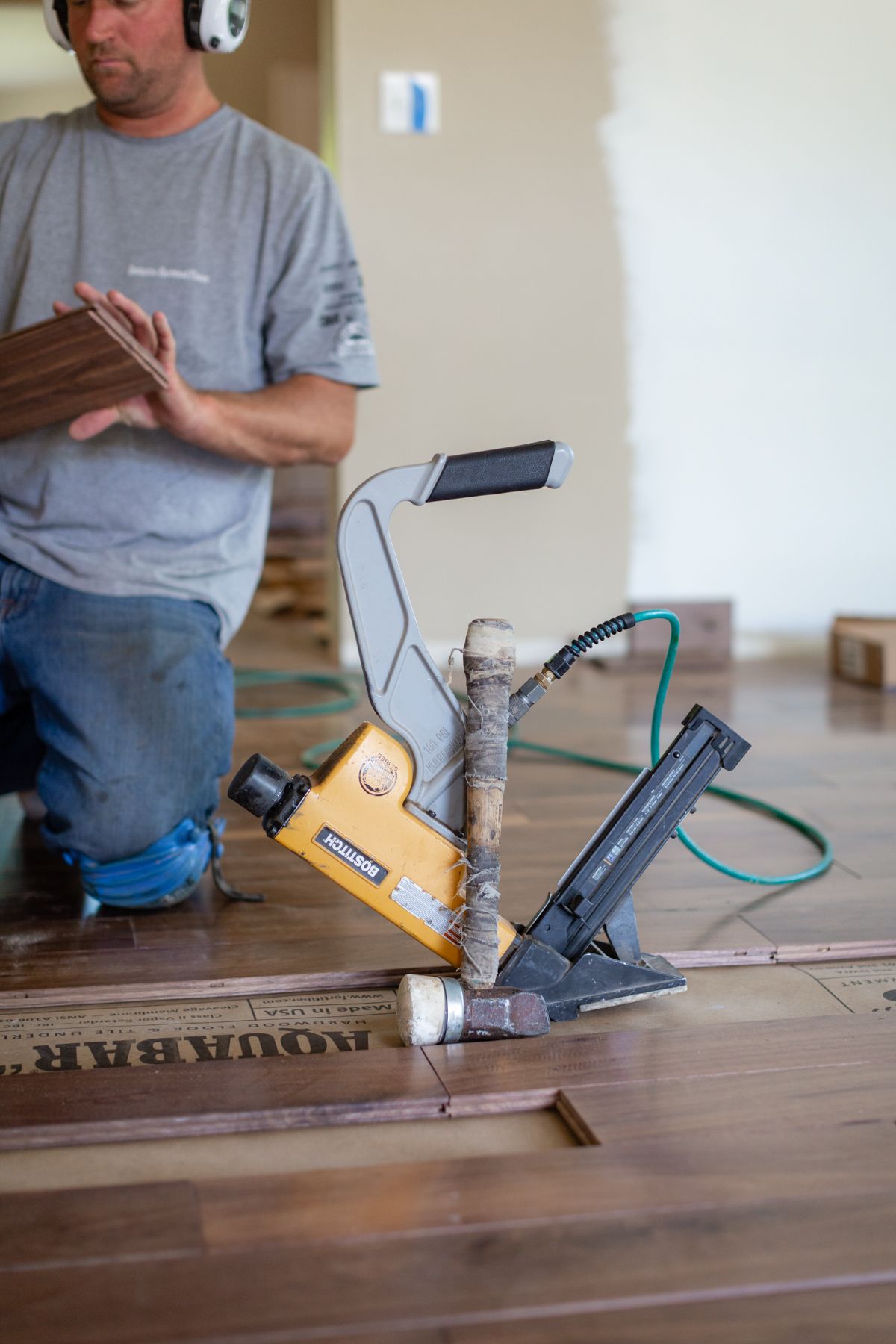Worker using a yellow floor nailer on a wooden floor during installation