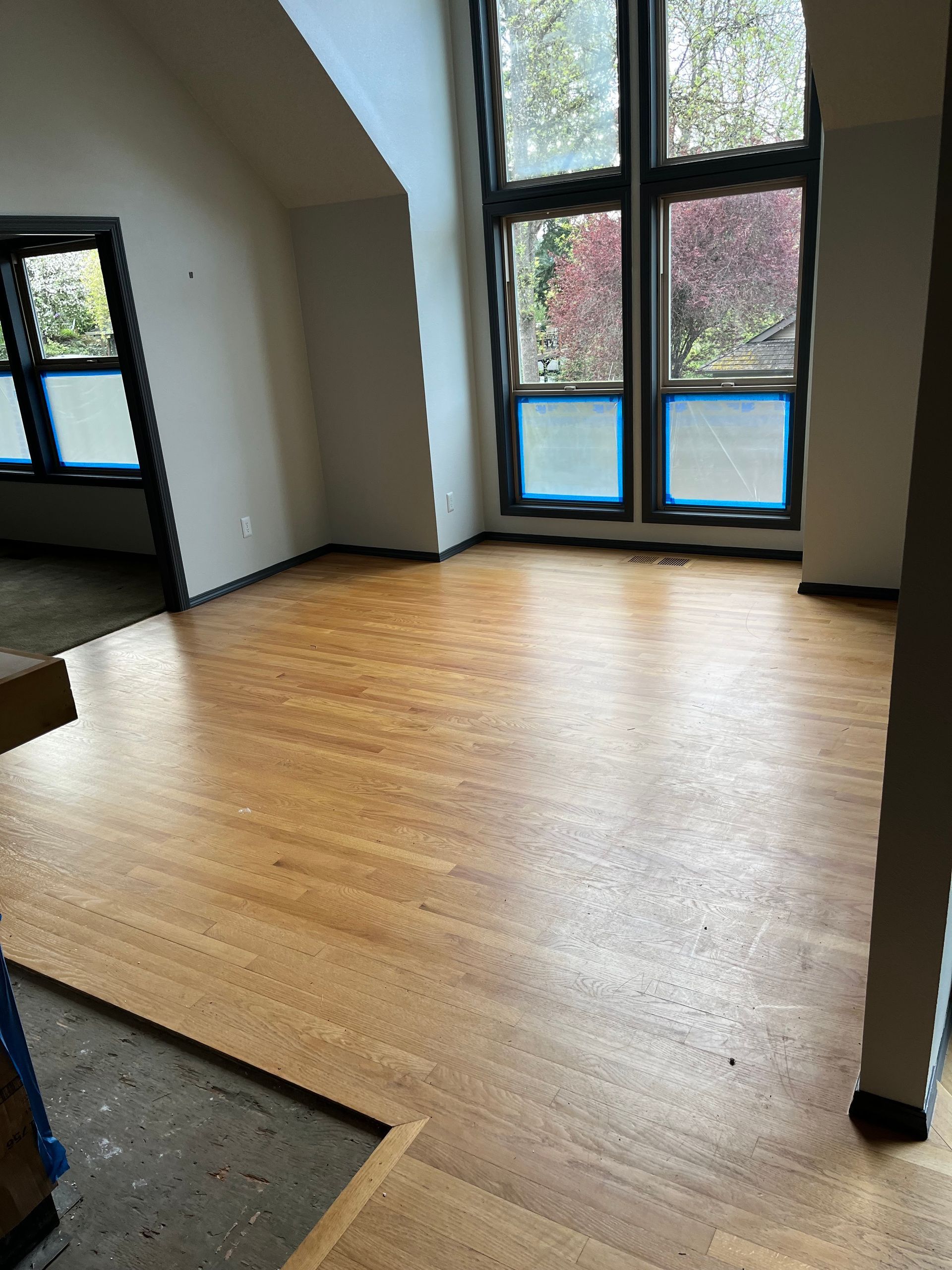 Empty room with light wood floor, tall windows, and white walls under slanted ceilings.