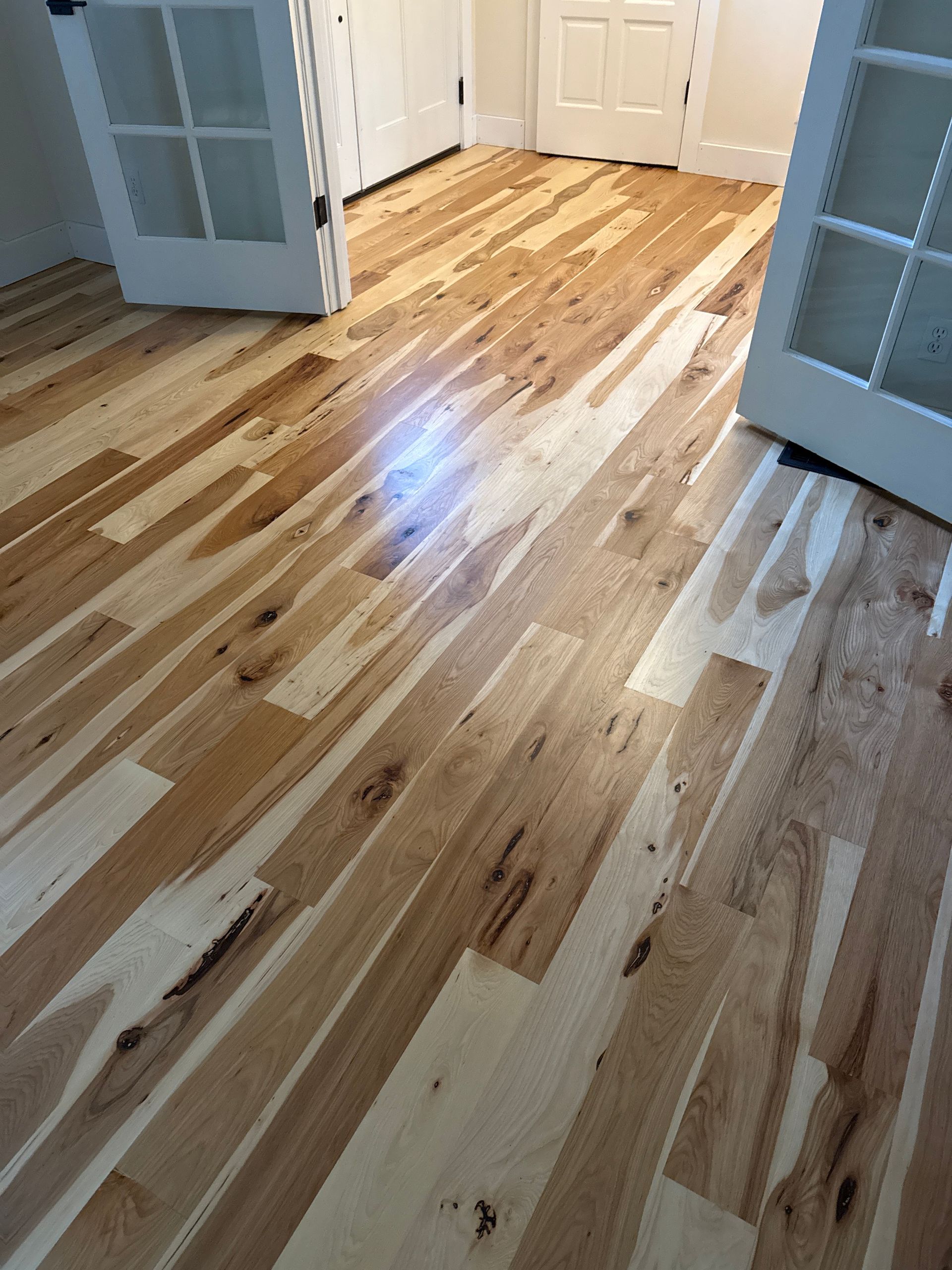 Polished light wood floor in a hallway with white doors and built-in cabinets.