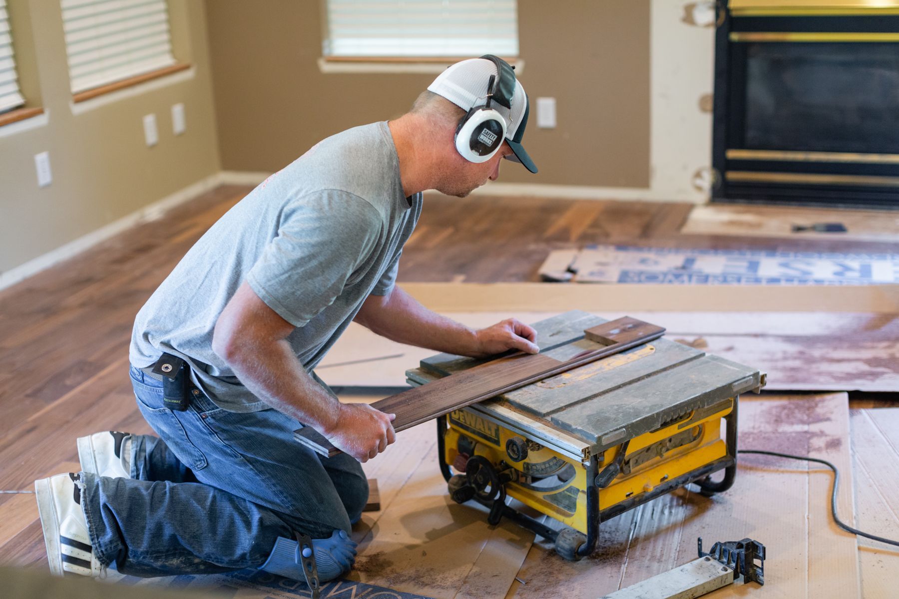Worker kneeling to cut wood flooring with a table saw in an empty room