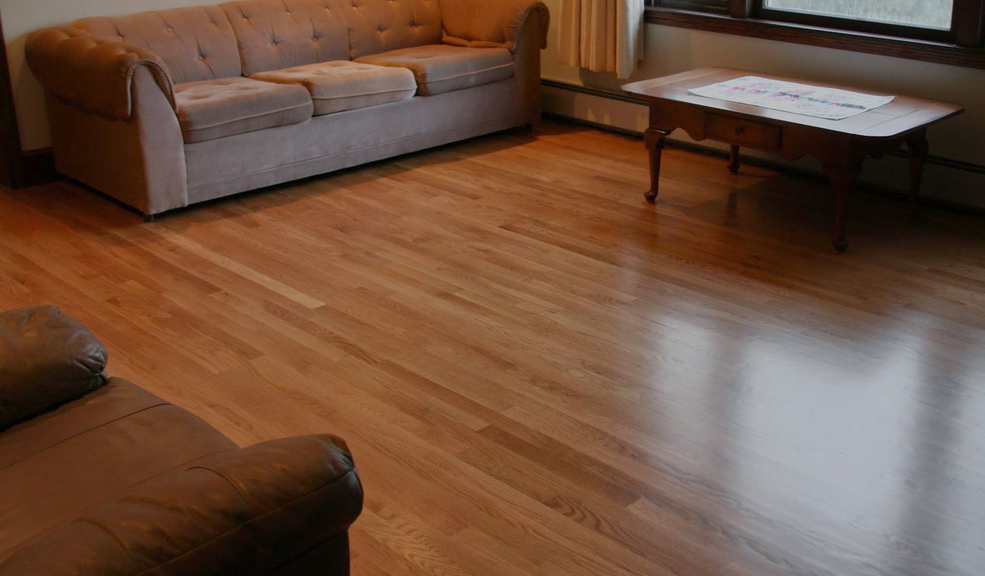 Living room with wooden floor, gray sofas, and a coffee table by a window.