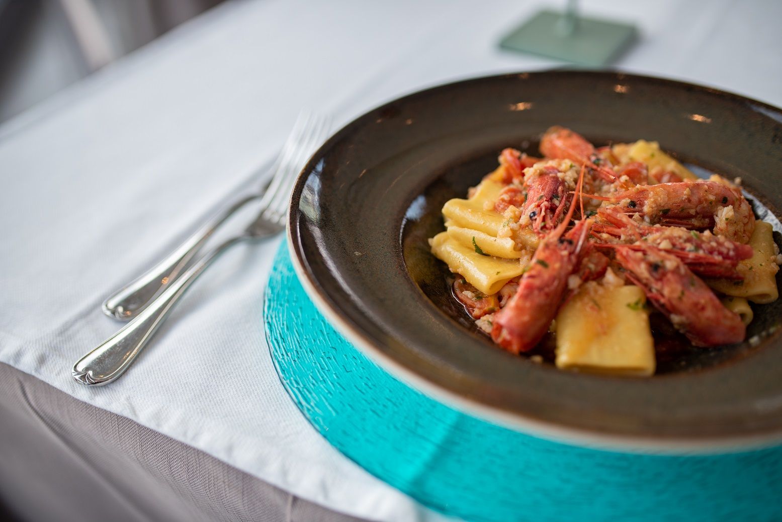Pasta al sugo rosso servita su un piatto scuro con tovagliolo turchese su una tovaglia bianca.