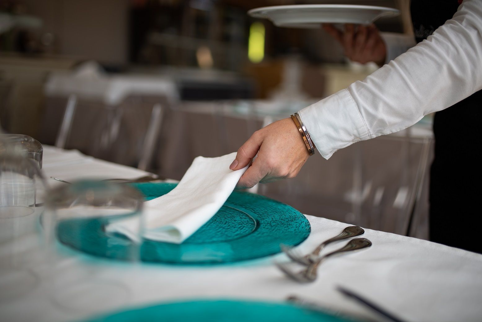 Una mano che posa un tovagliolo su una tovaglietta color verde acqua a un tavolo di ristorante.