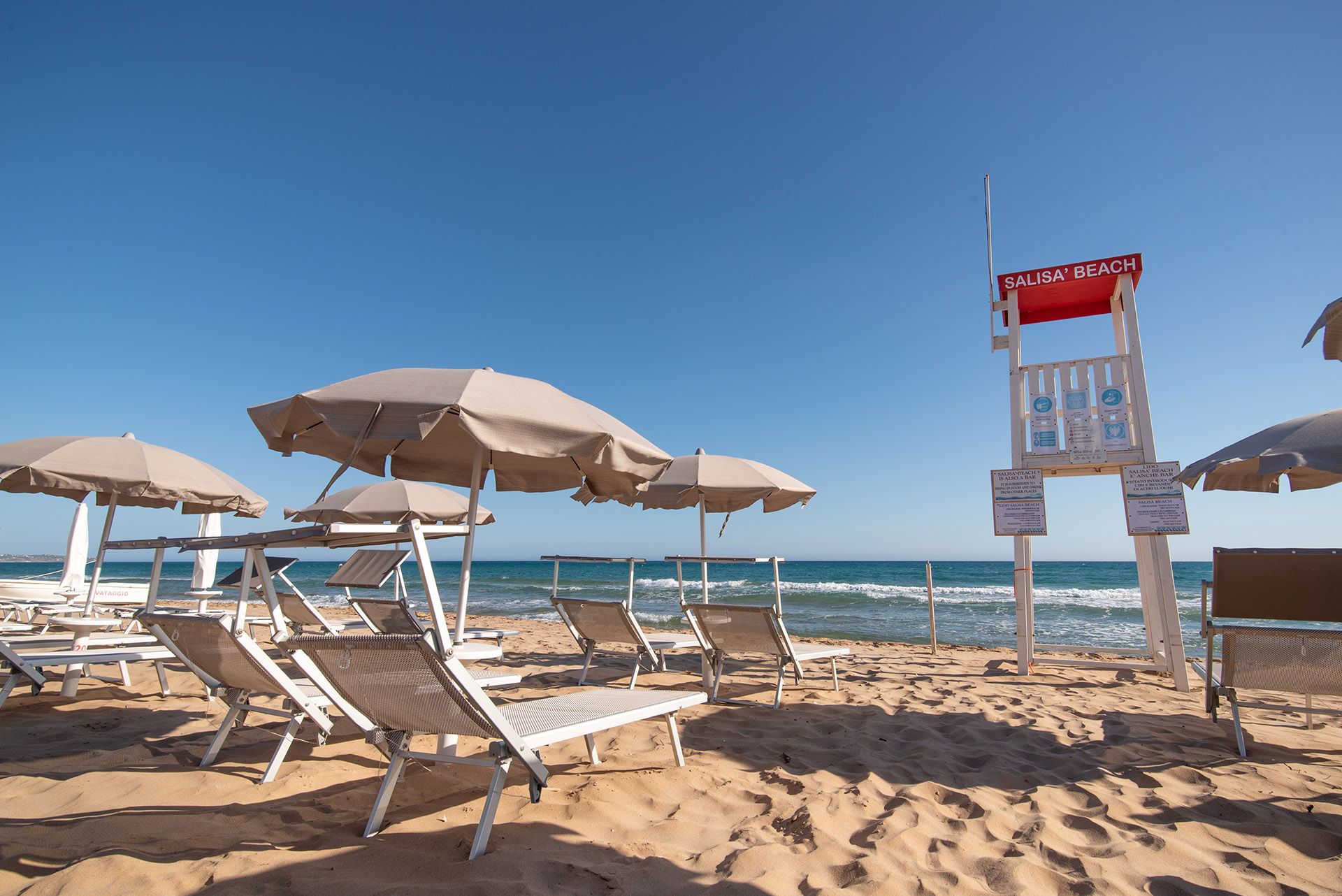 Beach with lounge chairs and umbrellas, with a lifeguard tower by the ocean under a clear blue sky