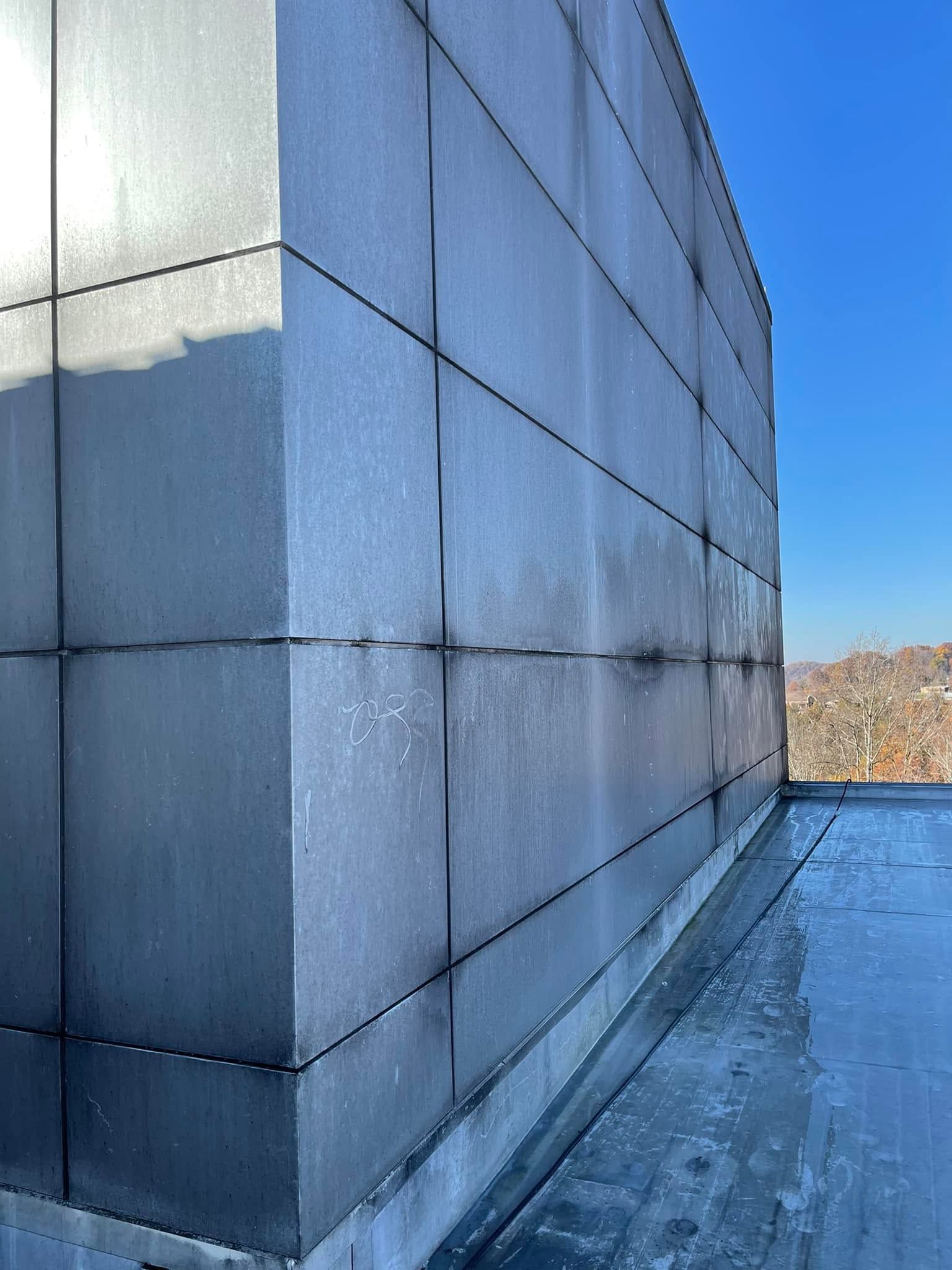 Blue metal-sided building corner beside a snowy rooftop under a clear sky