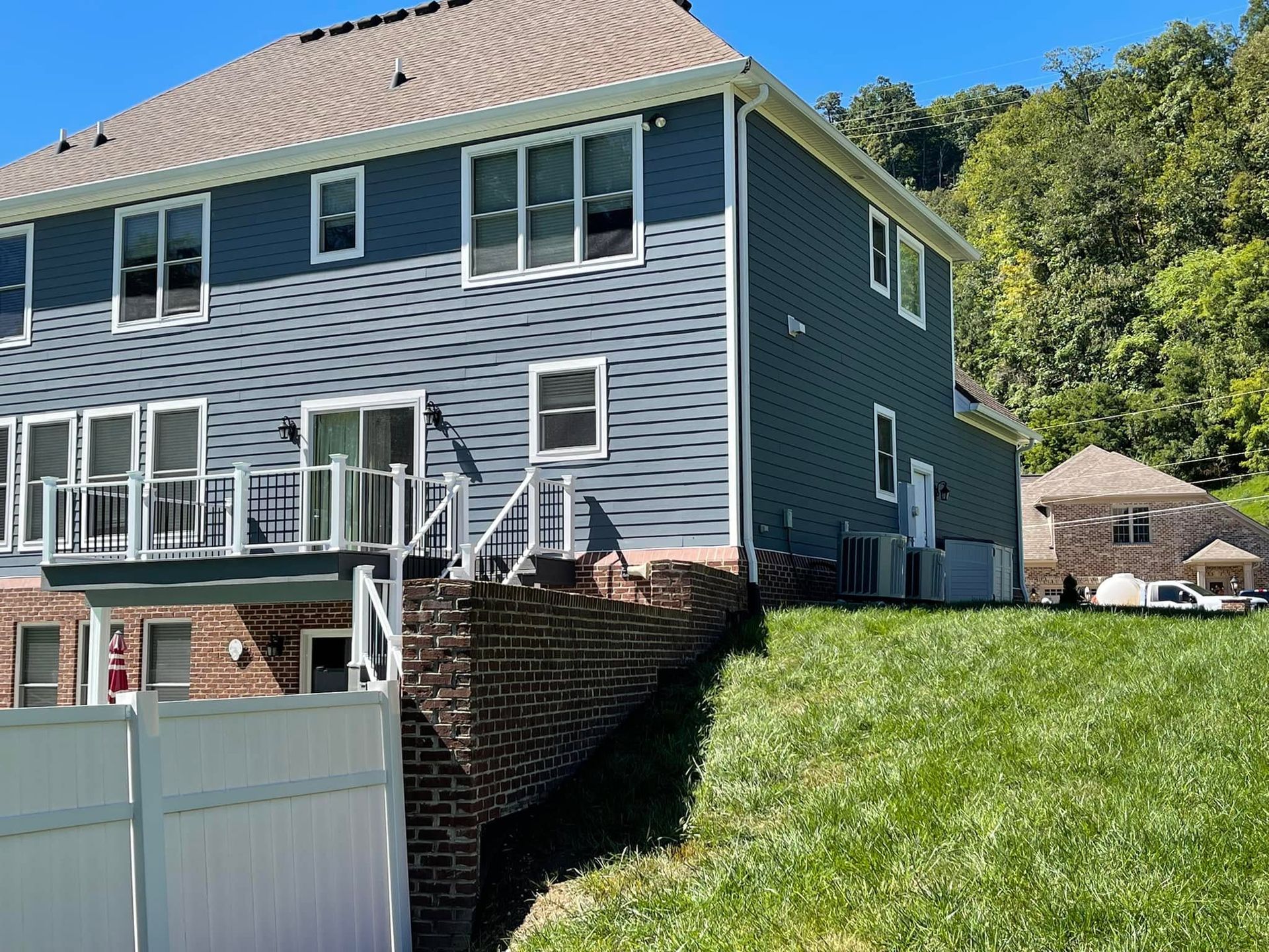 Blue two-story house with white trim and a grassy hillside in front