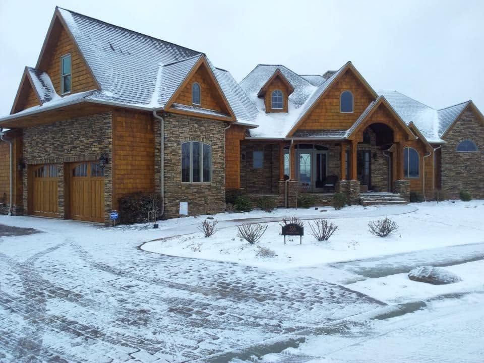 Snow-covered stone house with wooden gables and a curved driveway in winter