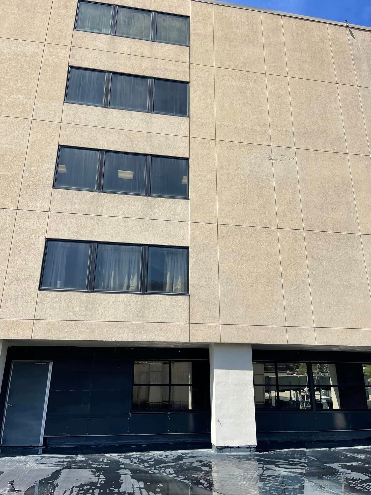Tan concrete apartment building with dark windows and street-level entrances, viewed from below