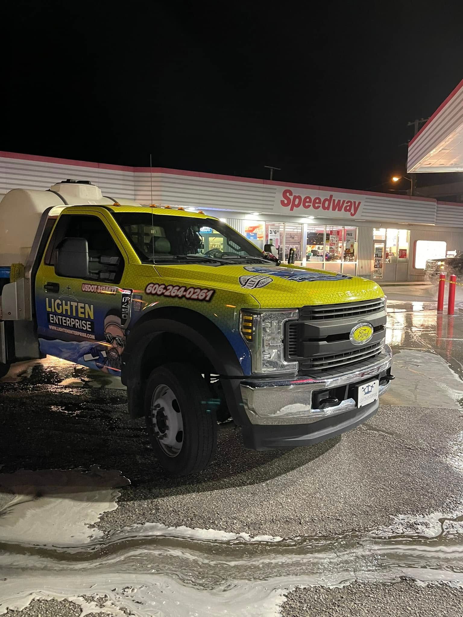 Yellow utility pickup truck parked outside Speedway gas station at night on wet pavement.