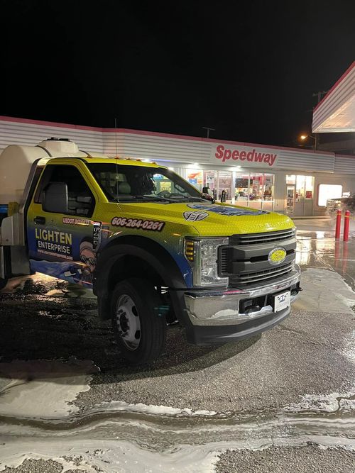 Yellow utility pickup truck parked outside Speedway gas station at night on wet pavement.