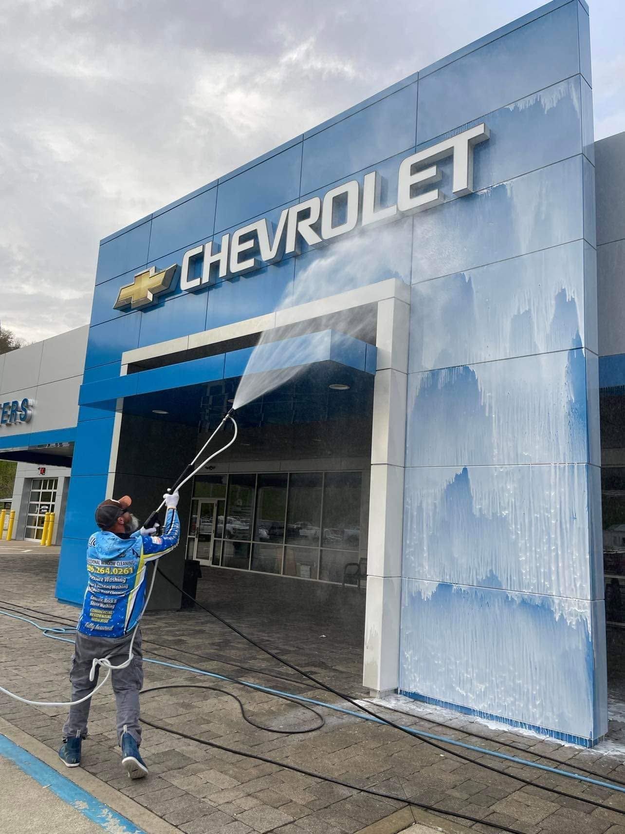 Person pressure-washes a Chevrolet dealership facade with blue soap foam.