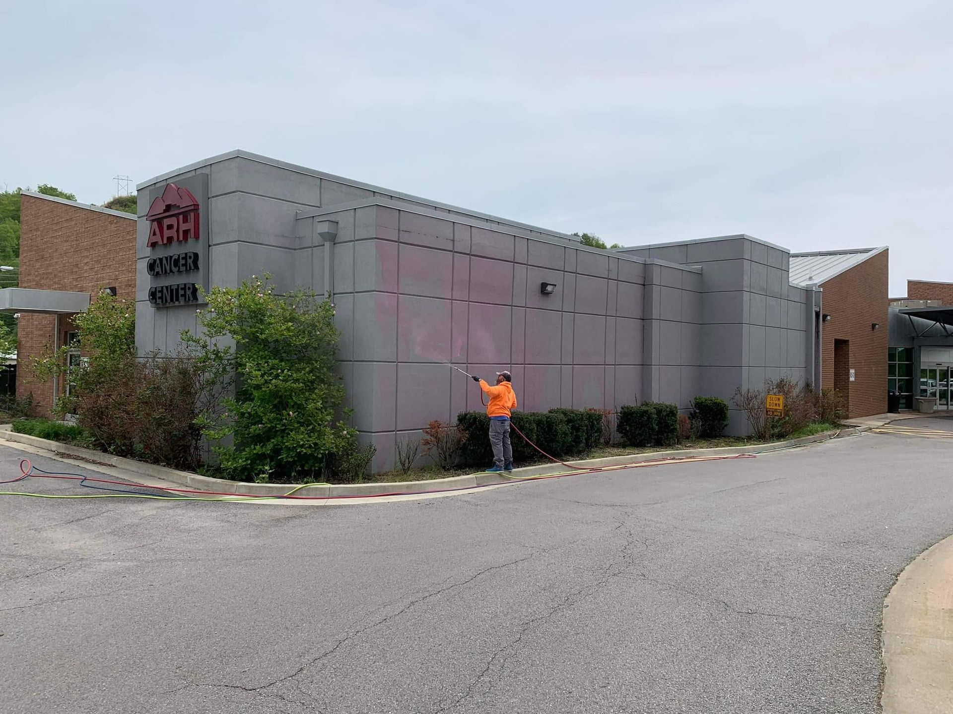 Person in orange vest standing outside a gray industrial building with signs.