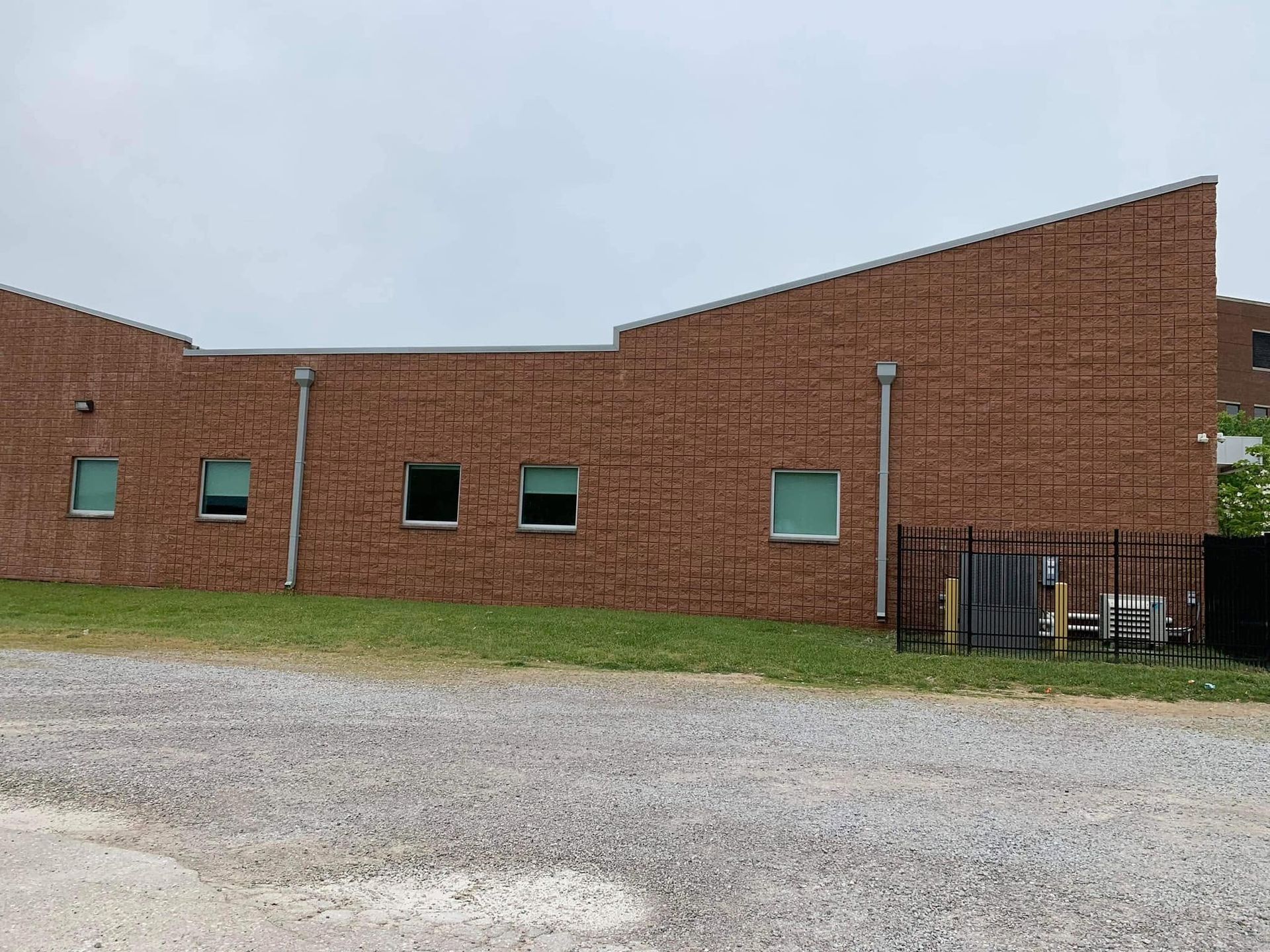 Brick building with a curved roof, small windows, and a fenced entrance beside a gravel lot.