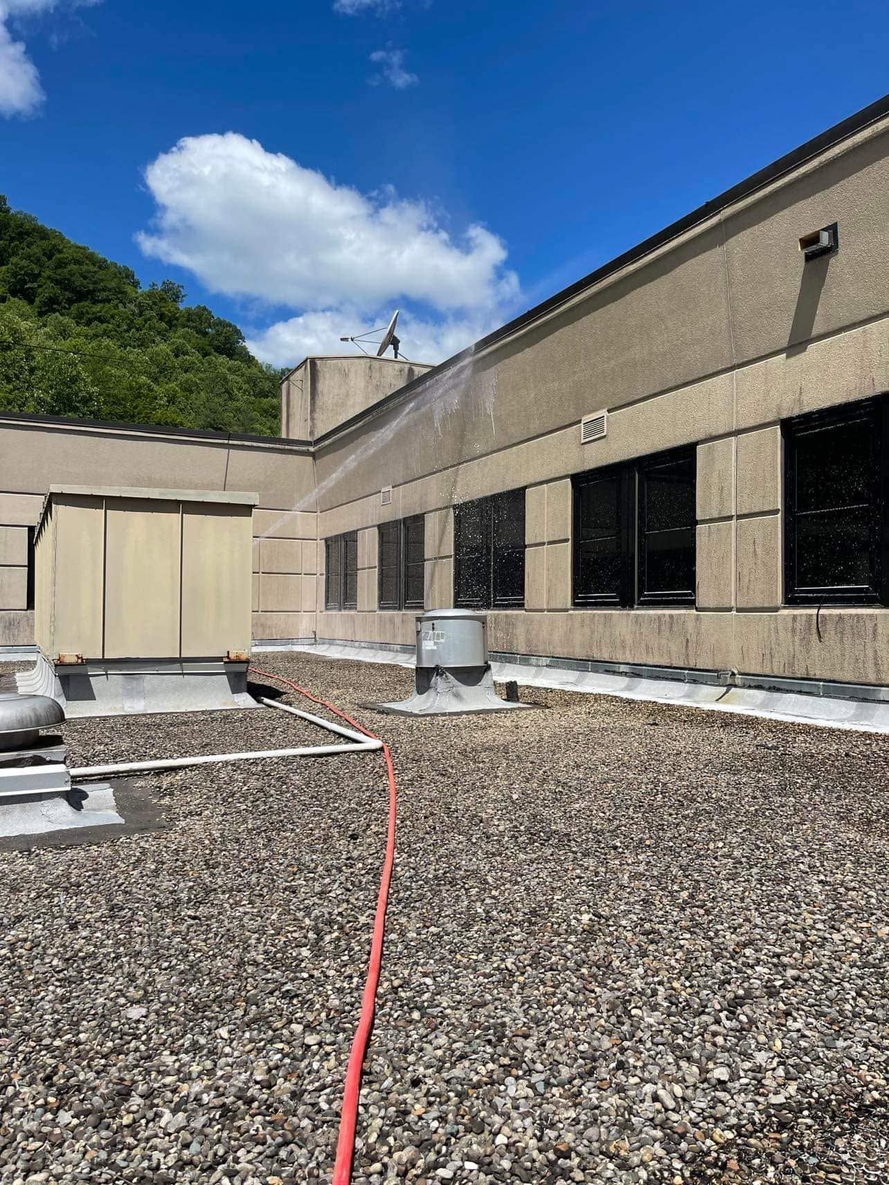 Rooftop with gravel surface, HVAC units, and a red hose beside a beige industrial building under a blue sky