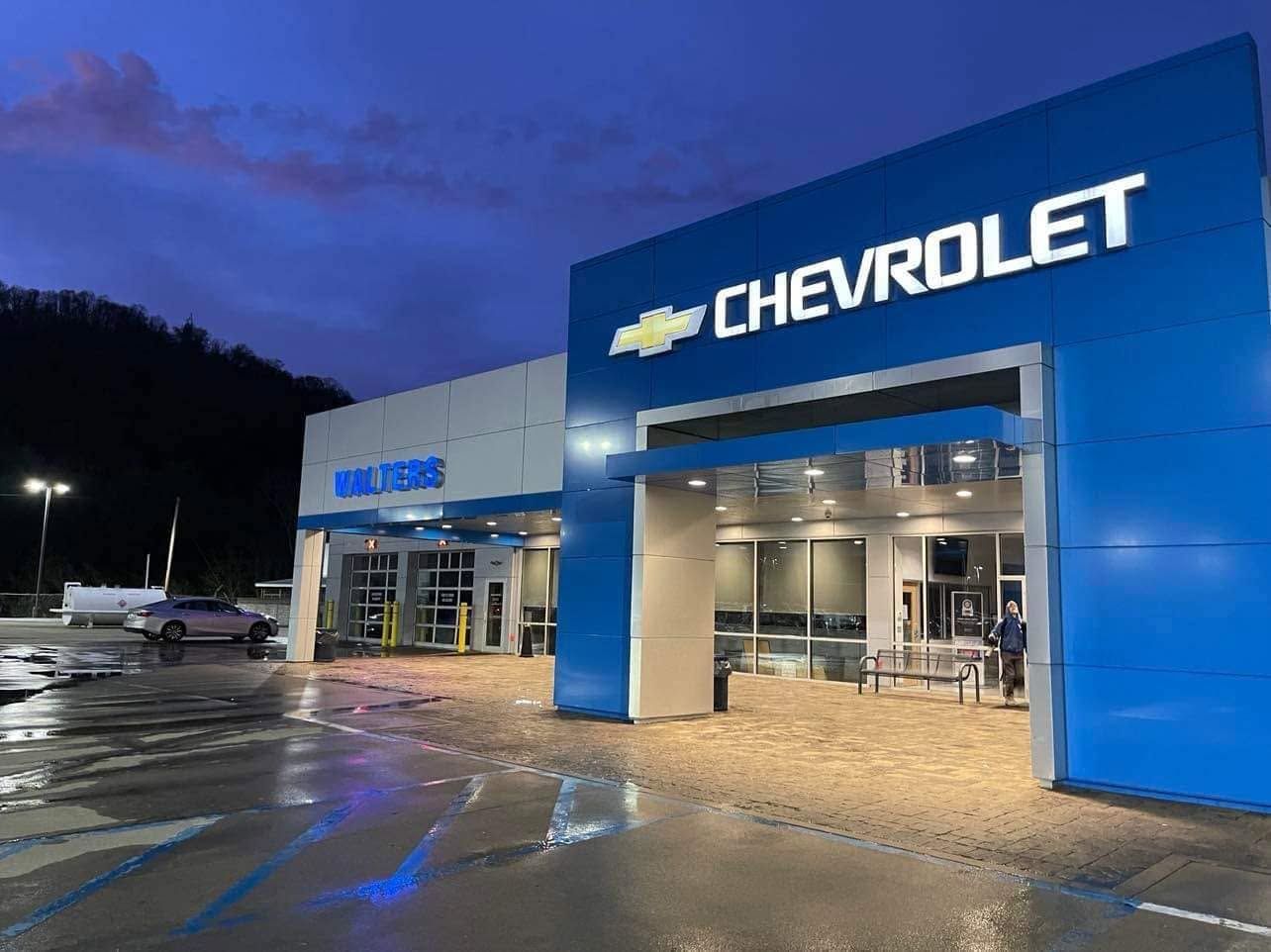 Chevrolet dealership exterior at dusk, with a bright blue facade and wet pavement reflecting the lights.