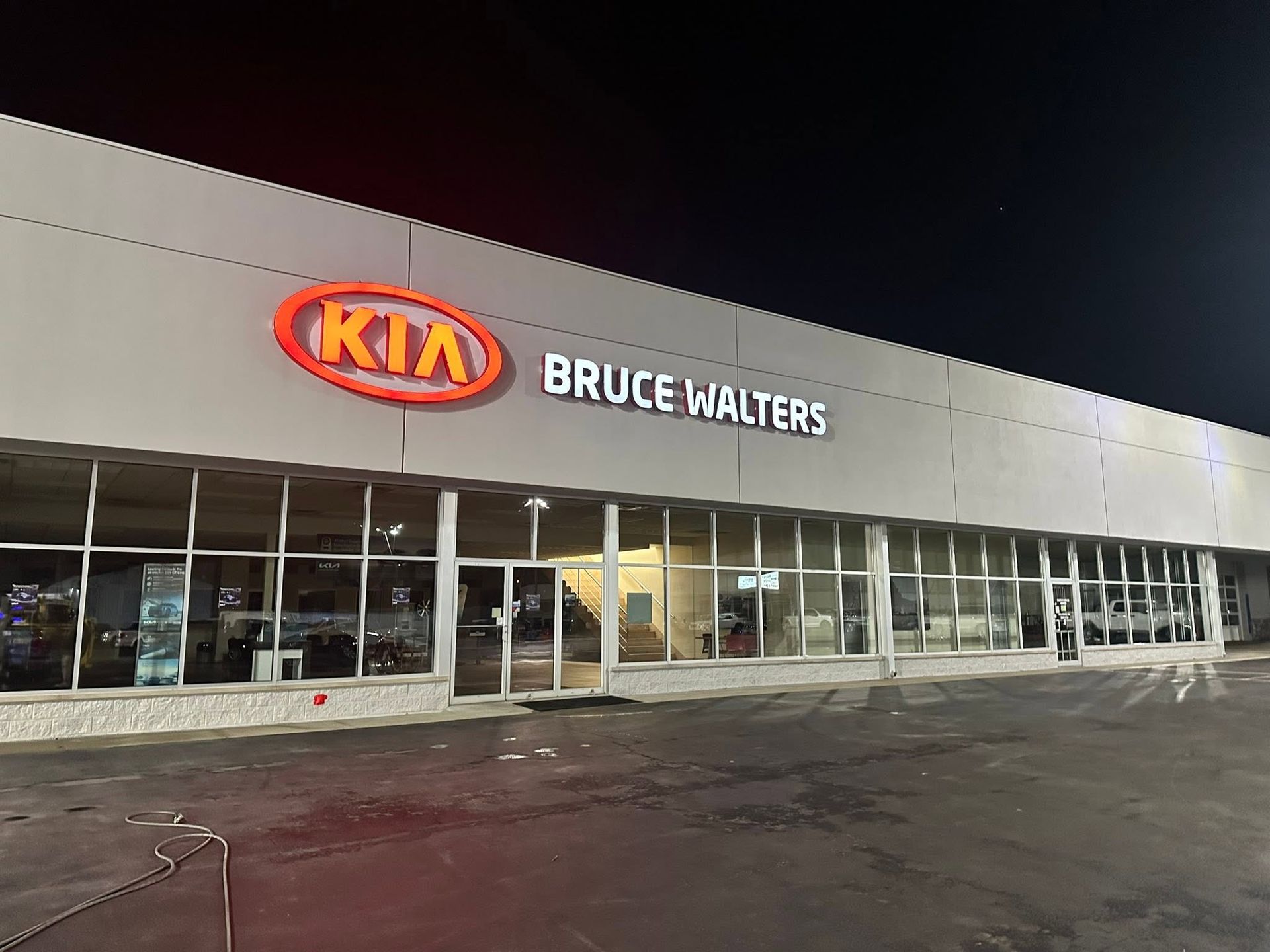 Kia dealership at night with illuminated Bruce Walters sign and glass storefront