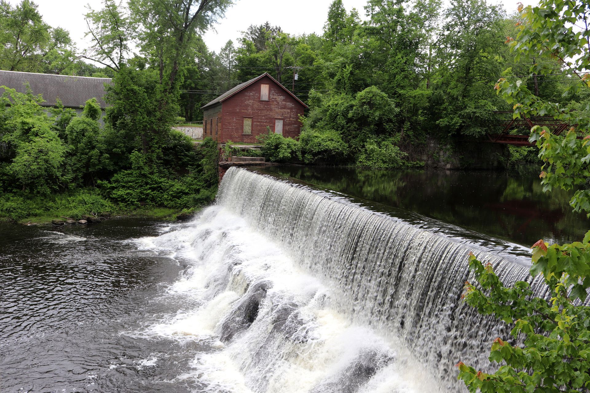 A waterfall is surrounded by trees and a house in the background.