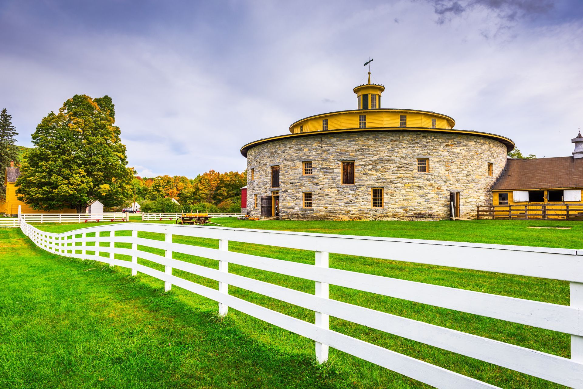 A round barn with a white fence in front of it.