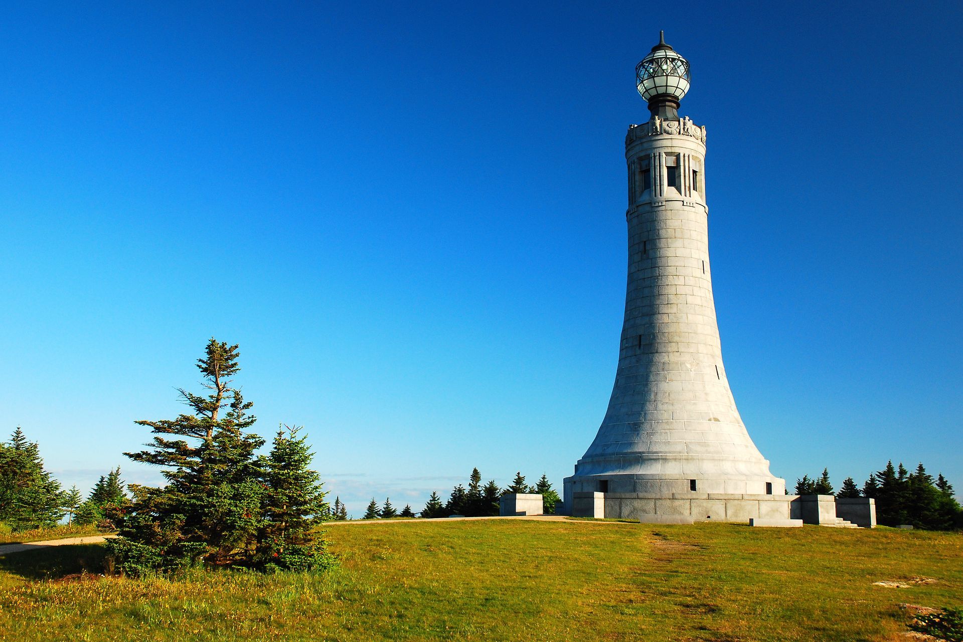 A large white tower is sitting on top of a grassy hill.
