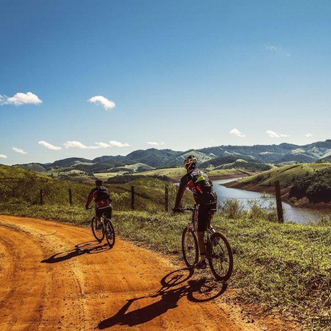 Two people are riding bicycles down a dirt road.