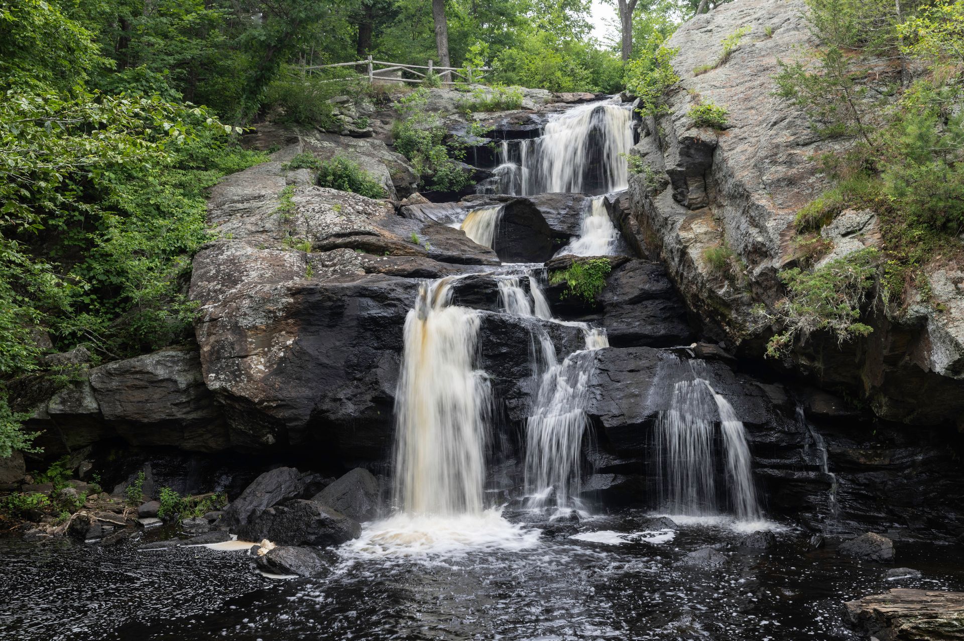Tiered waterfall cascading over dark rocks in a green forest setting