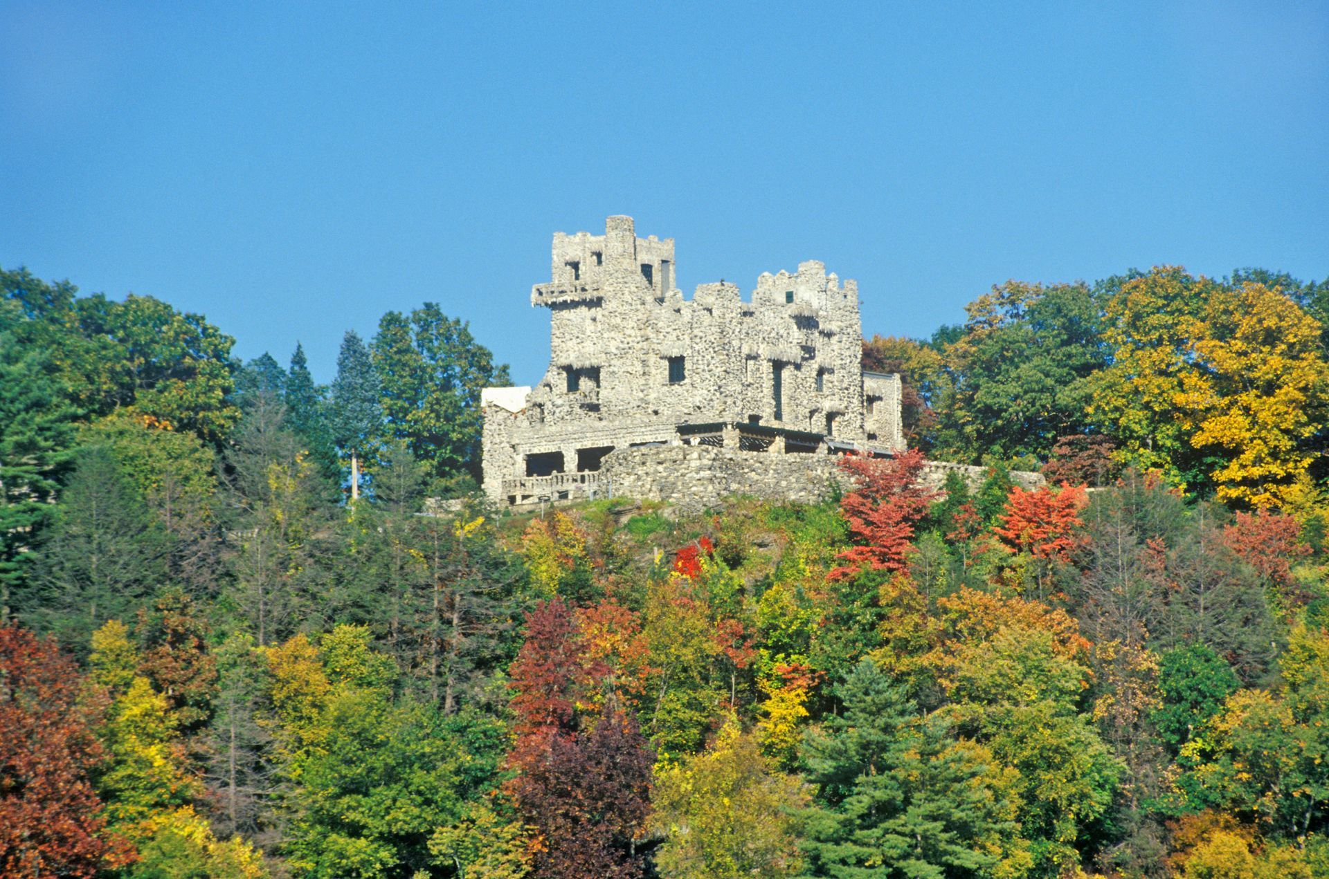 Stone castle on a forested hill with colorful autumn trees under a clear blue sky