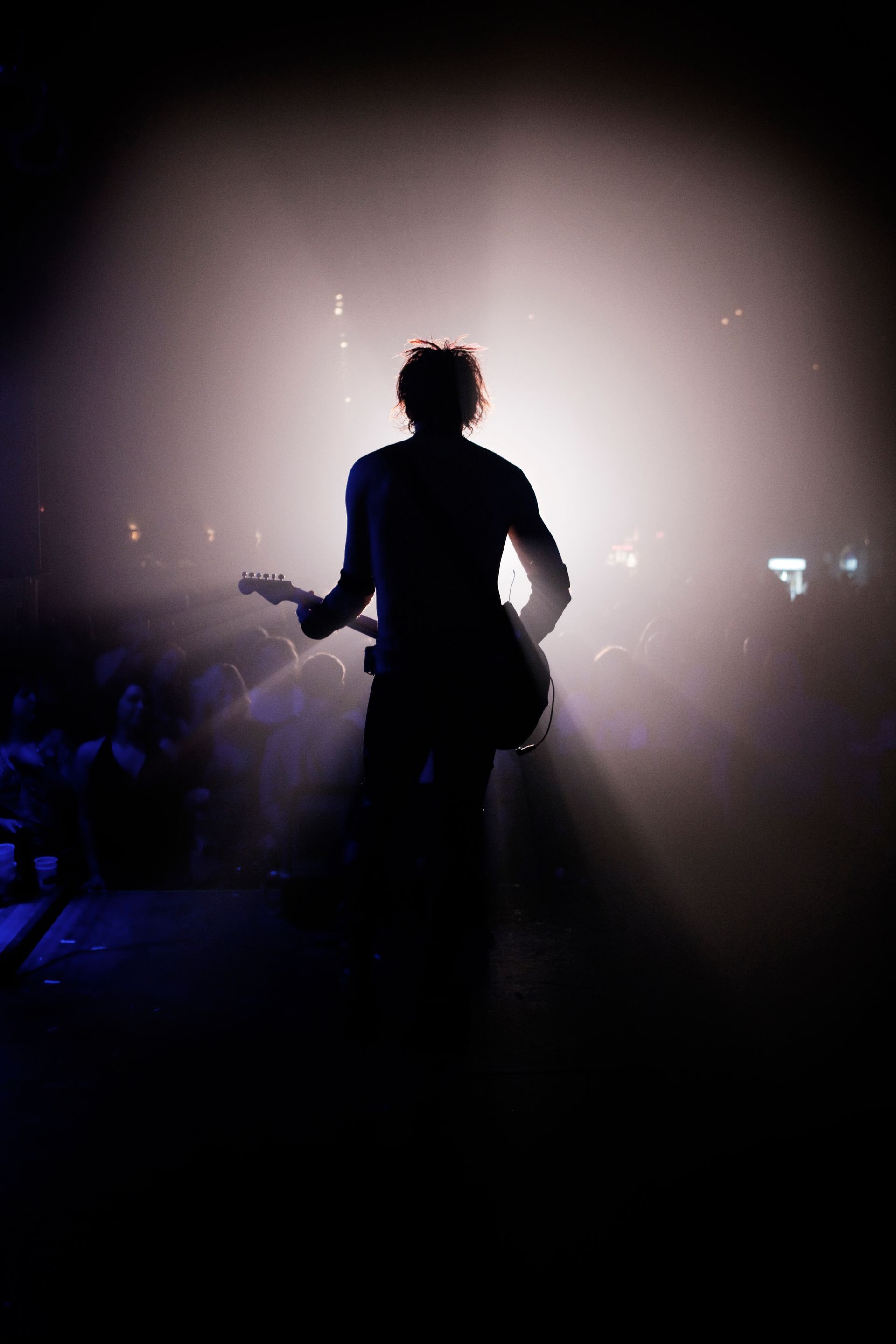 Silhouette of a guitarist on stage, lit by bright stage lights.
