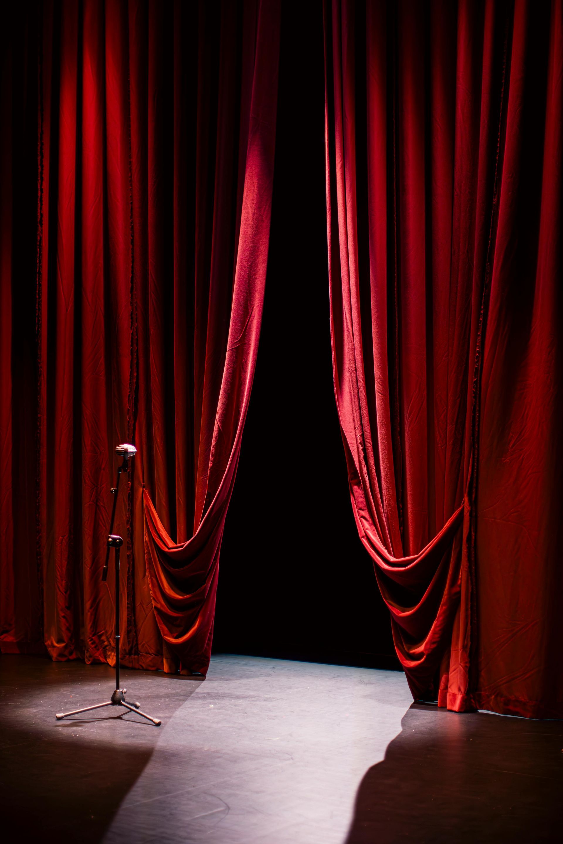 A microphone is sitting in front of a red curtain on a stage.