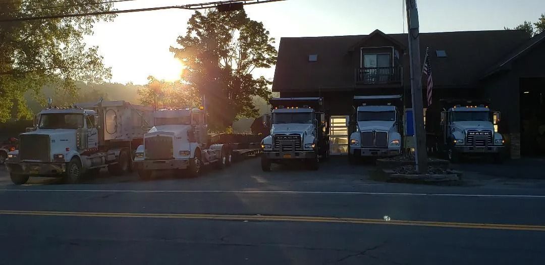 Trucks parked in front of a building, with the sun setting in the background.