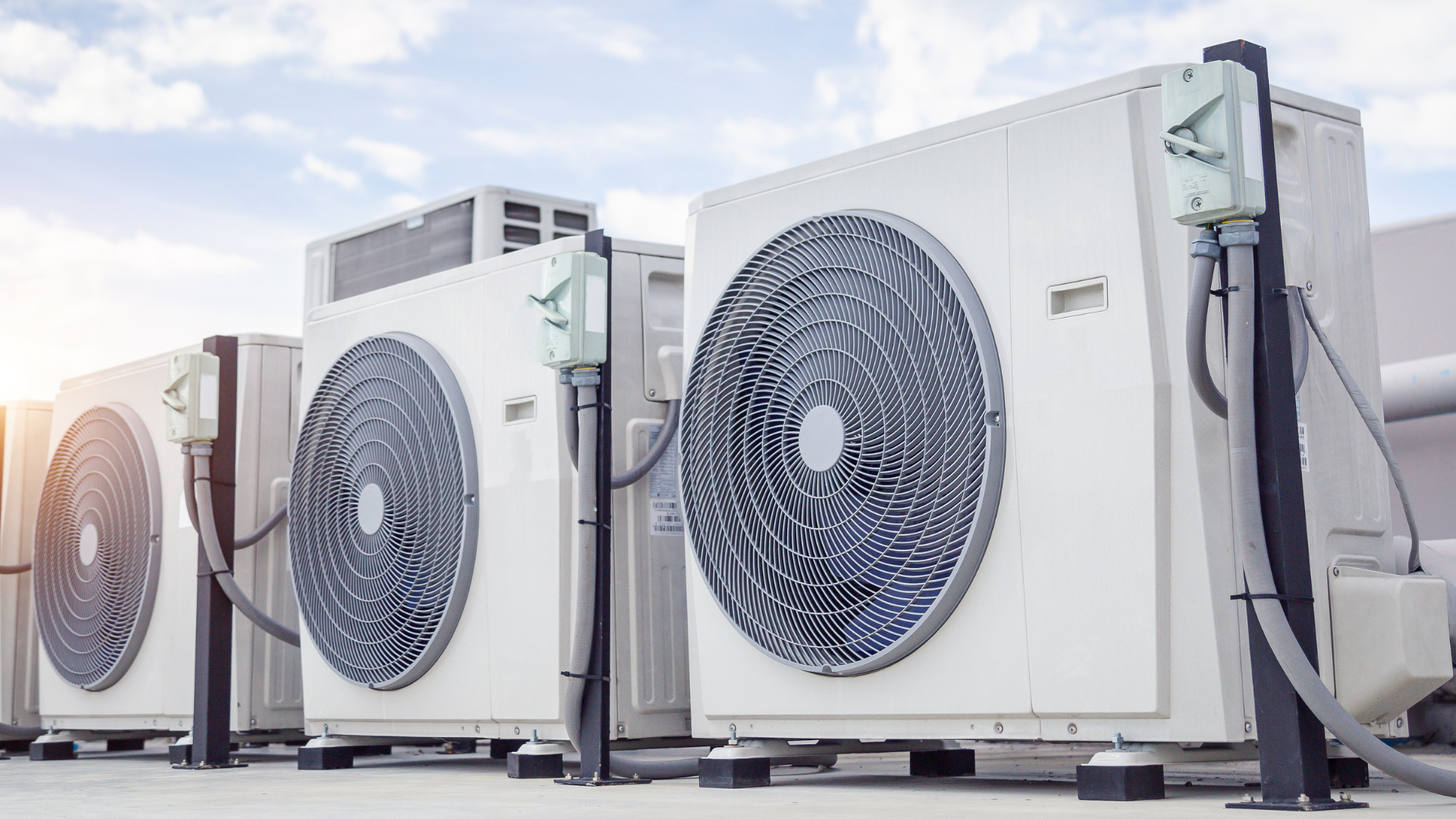 A gray HVAC unit sits on a flat, dark roof under a bright, clear sky.
