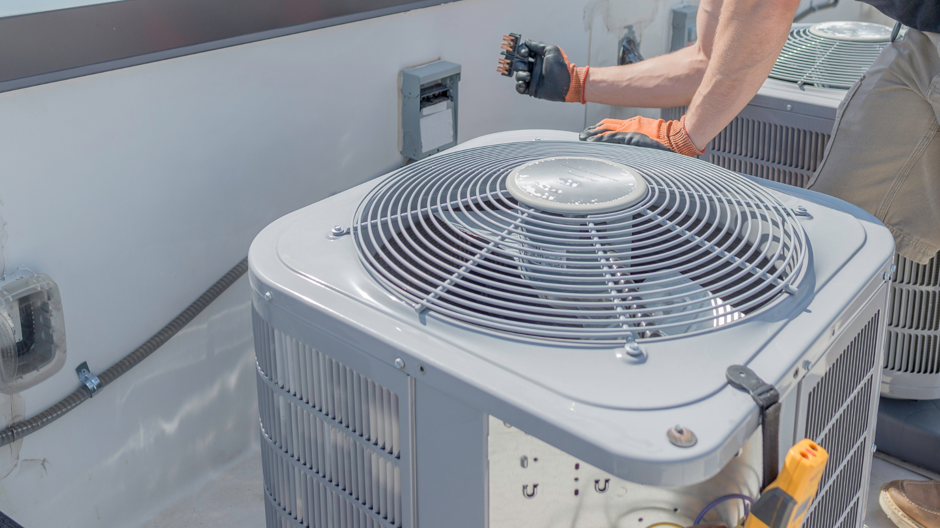 A person wearing glasses and a mask uses a gauge manifold to service an outdoor air conditioning unit.