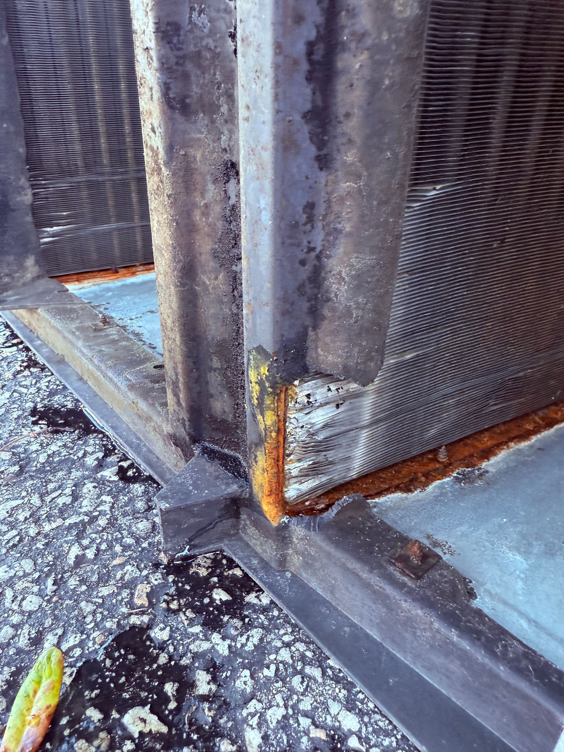 Close-up of a damaged HVAC evaporator coil showing significant rust and corrosion along the base and metal frame.