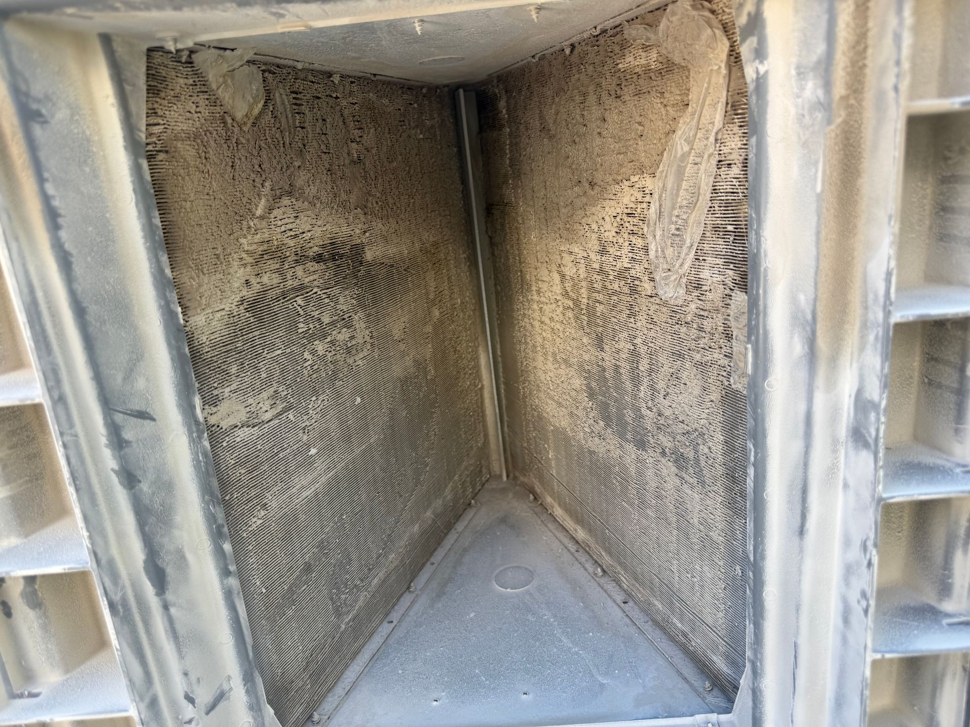 An HVAC A-coil evaporator unit heavily coated in thick dust and gray grime.