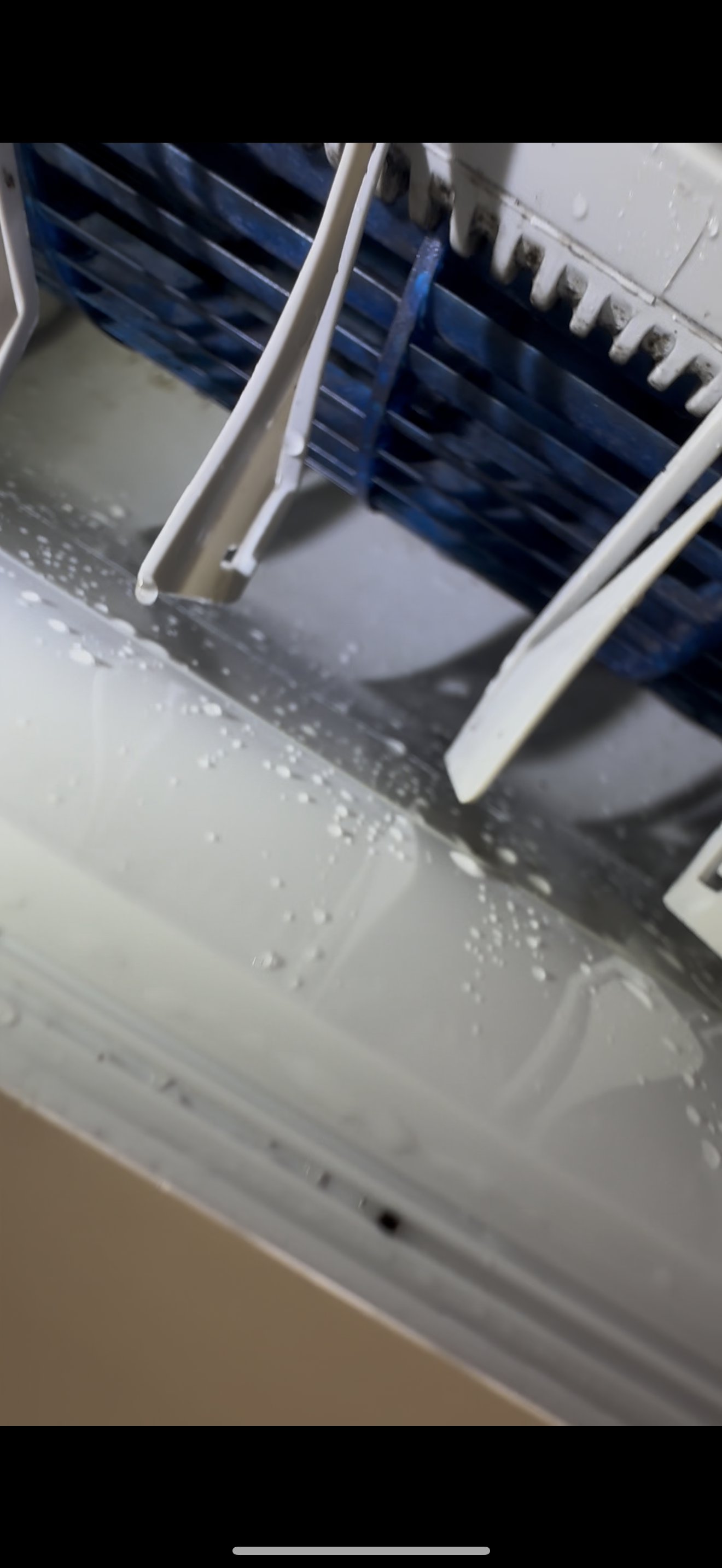 Close-up of a white air conditioner vent spraying fine, misty water droplets from its blue inner slats.