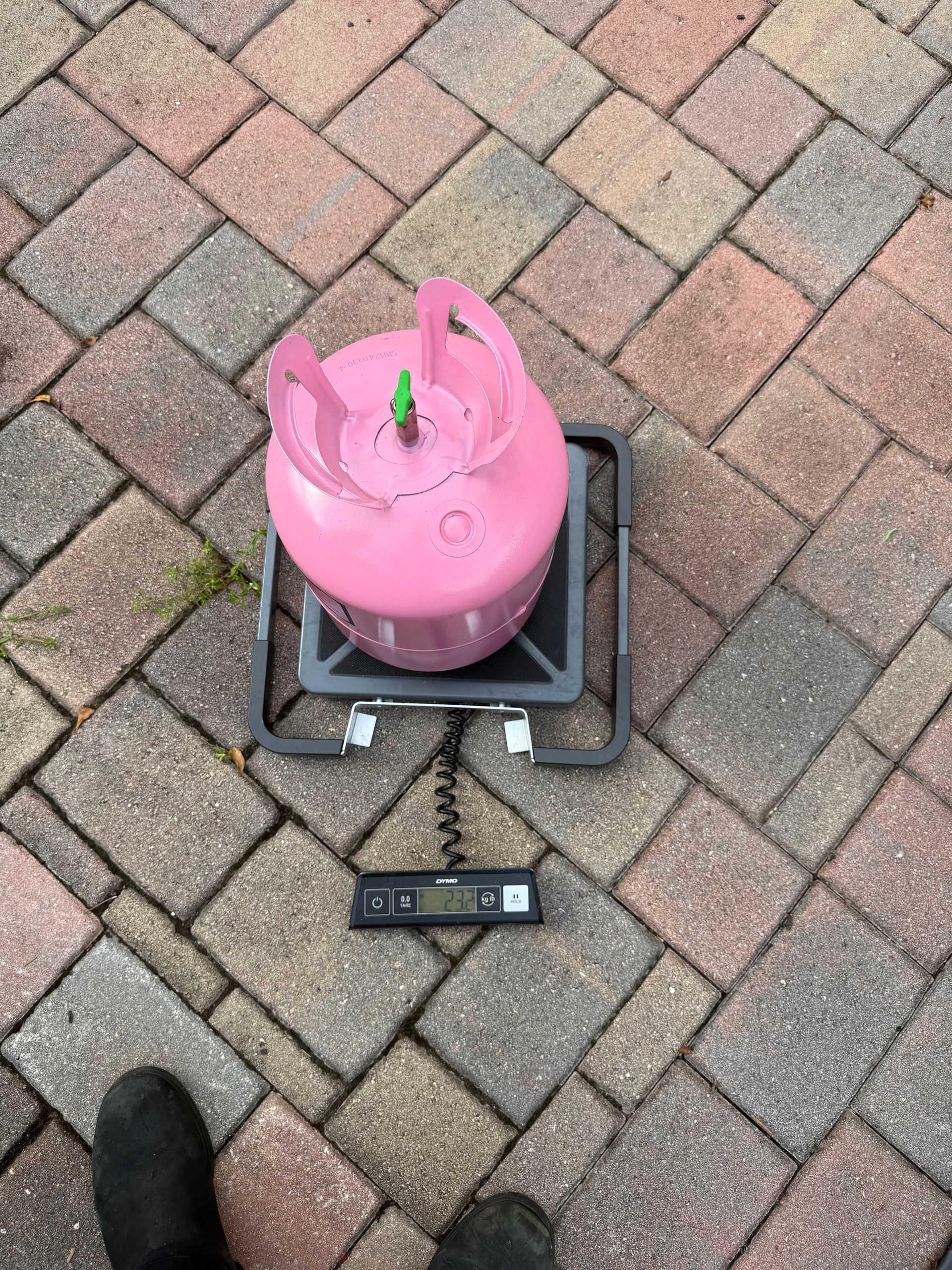 A pink refrigerant tank sitting on a digital scale placed on a brick patio.
