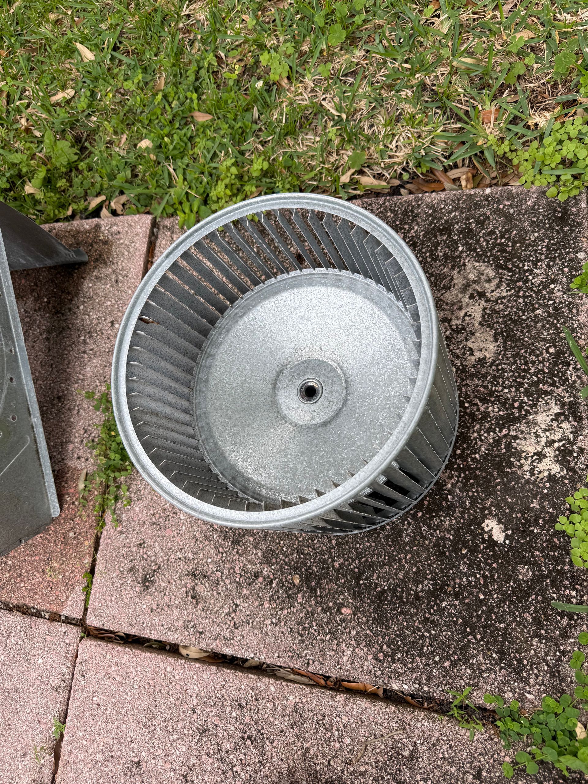 A metal blower wheel from an HVAC system sits on outdoor patio pavers.