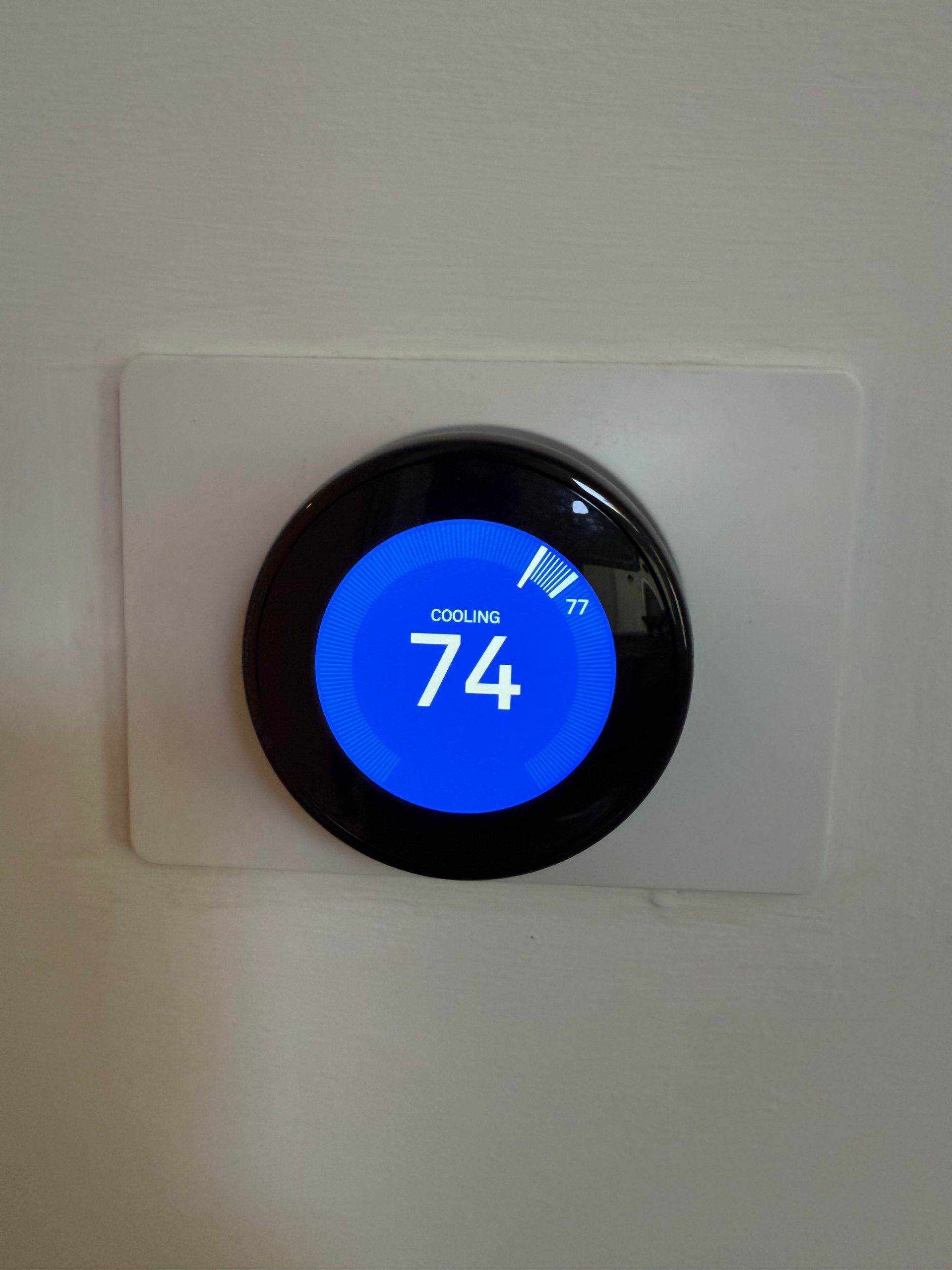 A Google Nest thermostat mounted on a white wall, displaying a current temperature of 74 degrees with a blue background.
