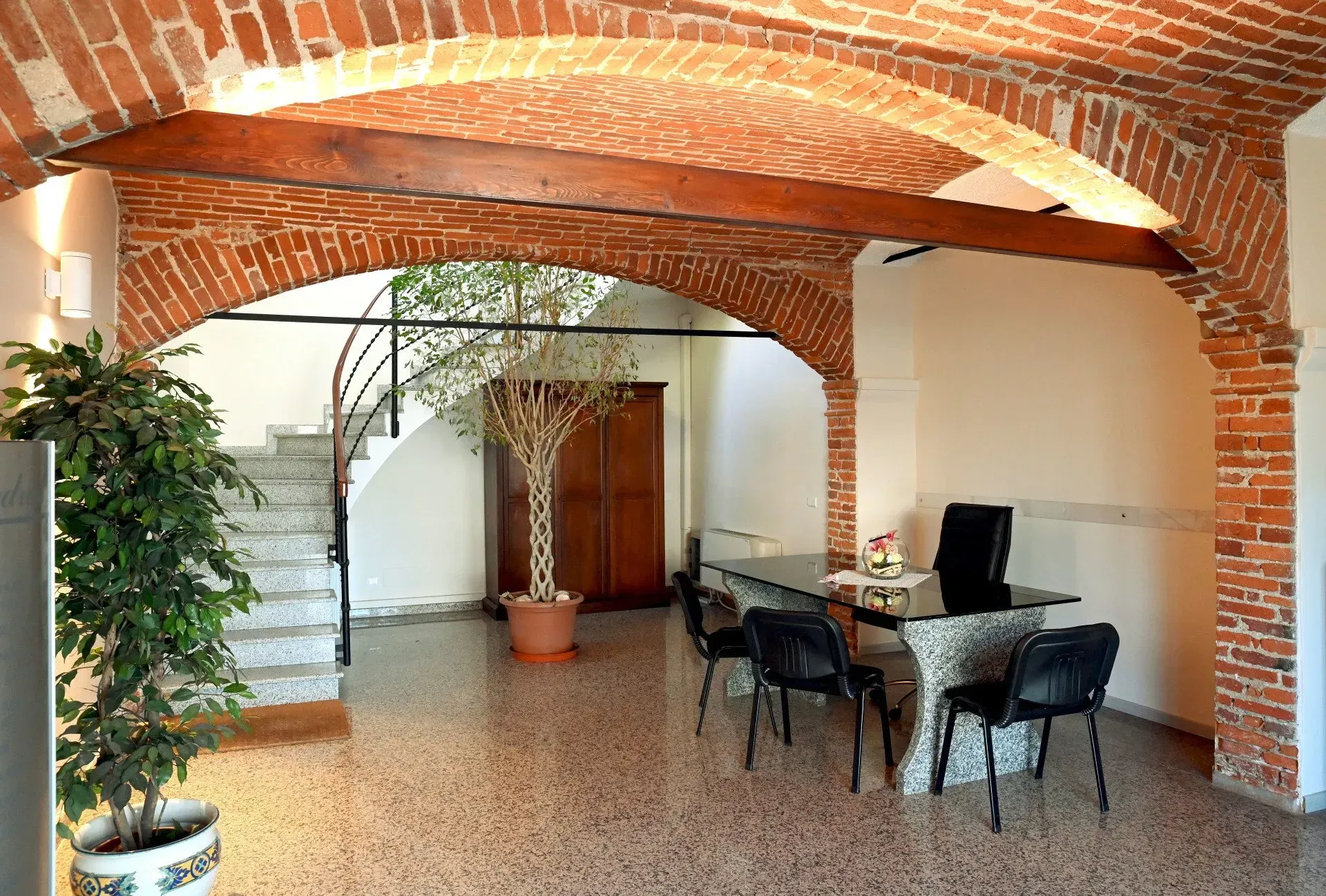 Interno con archi in mattoni, pavimento in terrazzo, scala e una scrivania con sedie.