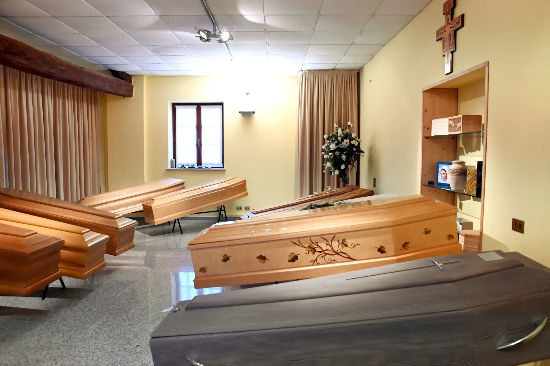 Interno di un'agenzia di pompe funebri, numerose bare chiuse in esposizione.