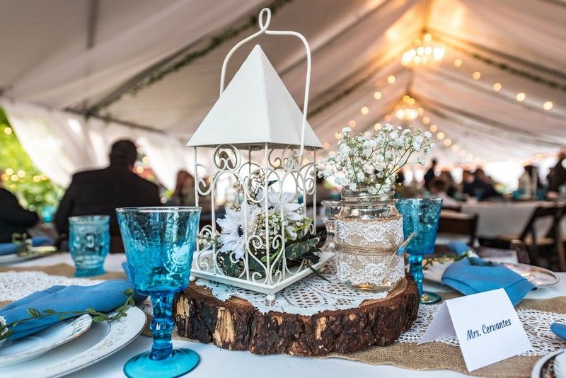 A table set for a wedding reception with blue glasses and a white lantern on a wooden stump.