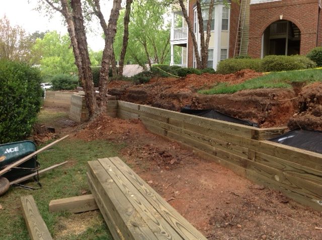 Wooden retaining wall being built near a building, with exposed dirt and construction materials.