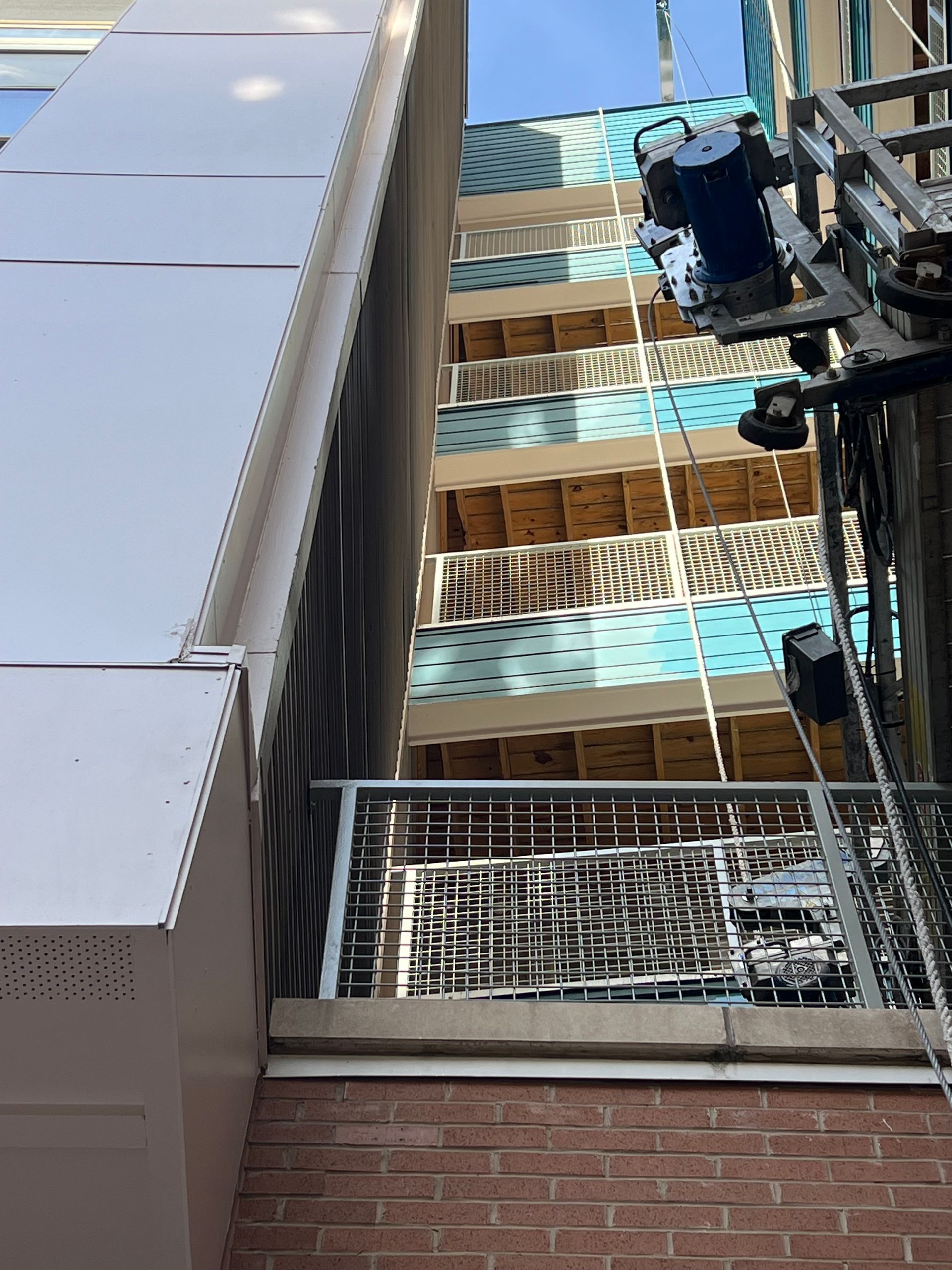 Building facades, some teal and brown brick, with a balcony and an industrial lift in between.