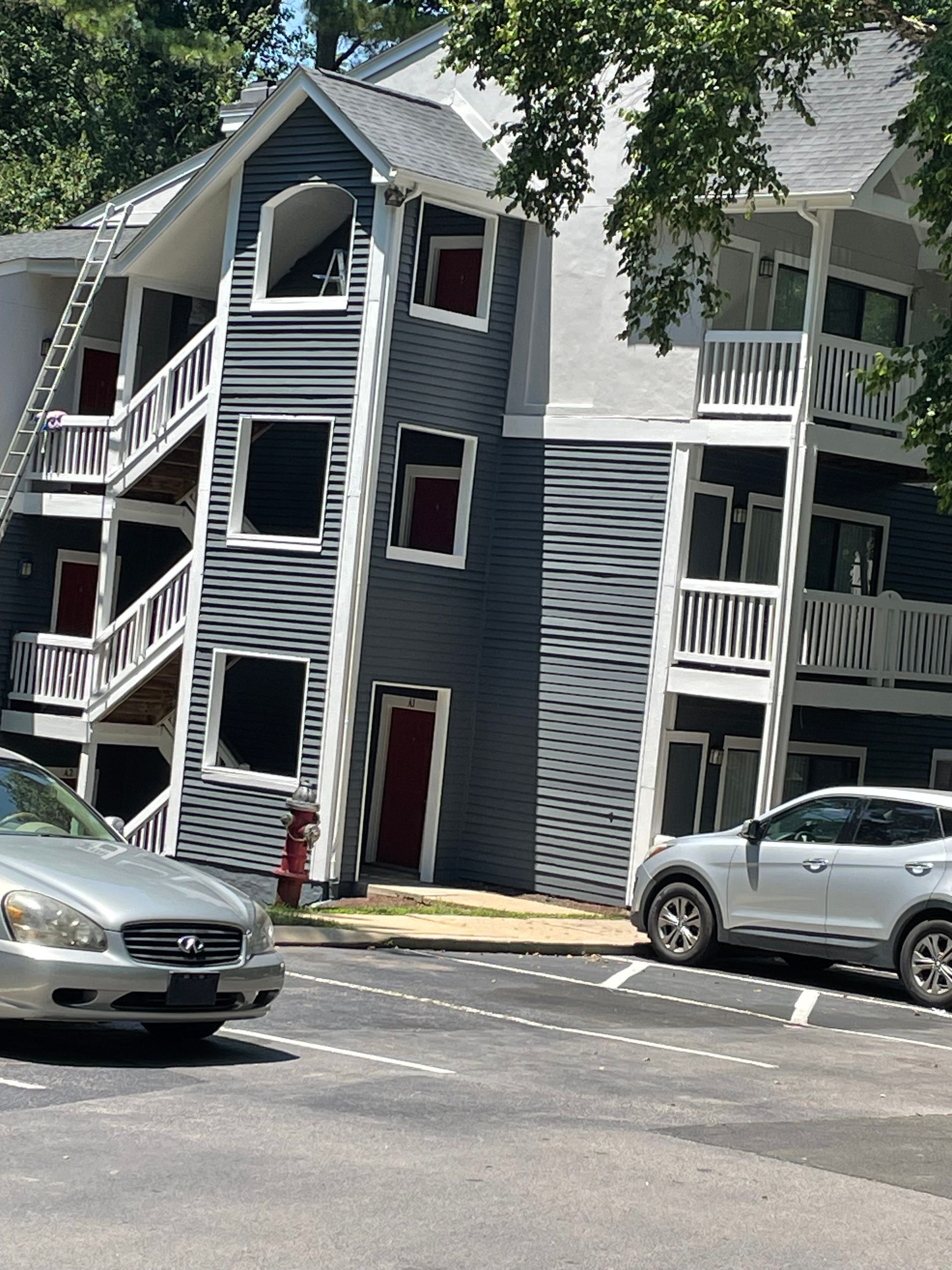Apartment building with gray siding, red doors, and exterior staircases; cars parked in front.
