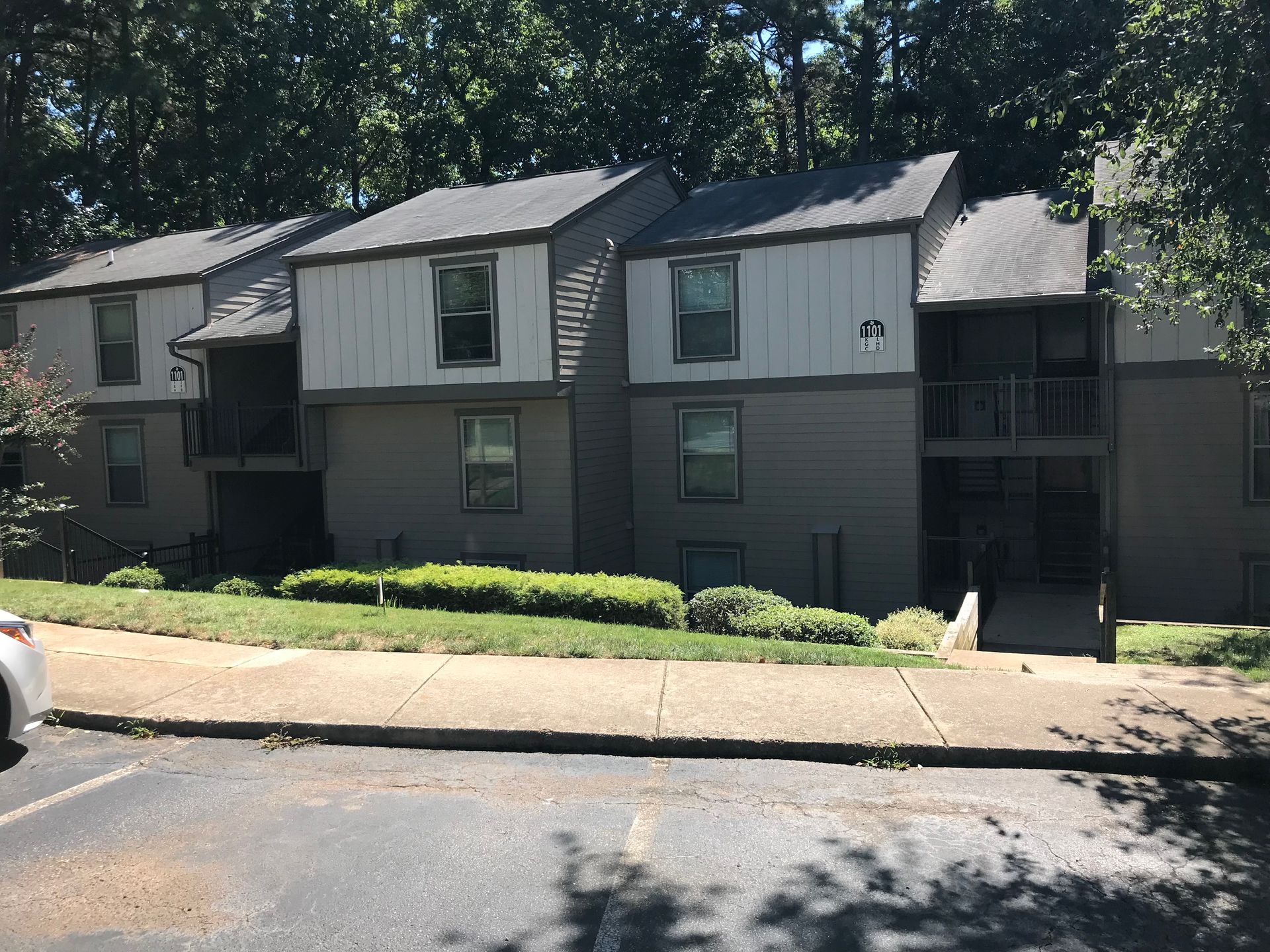 Apartment building with gray and white facade, surrounded by trees and a sidewalk.