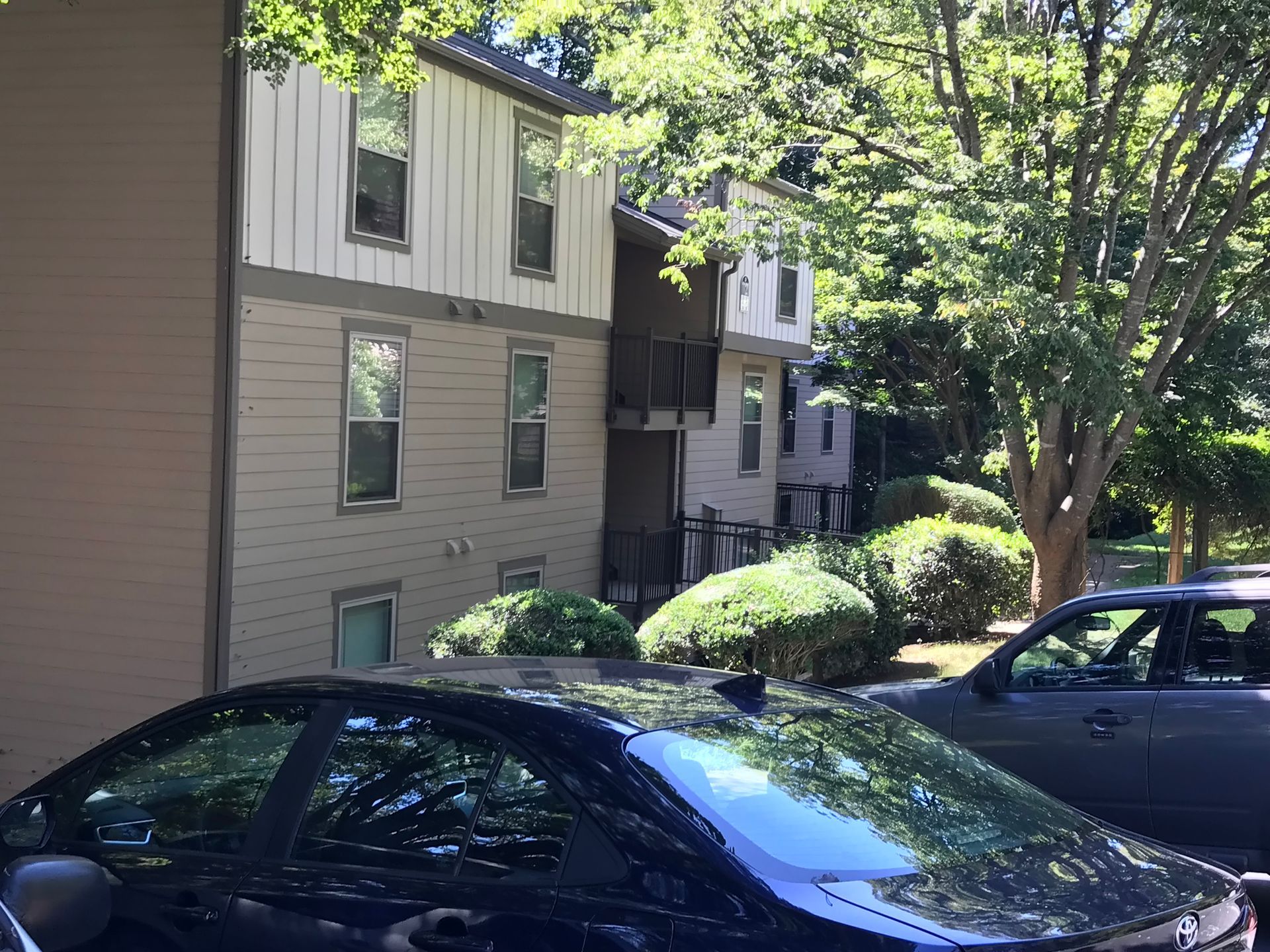 Apartment building with tan siding and dark cars parked in front.